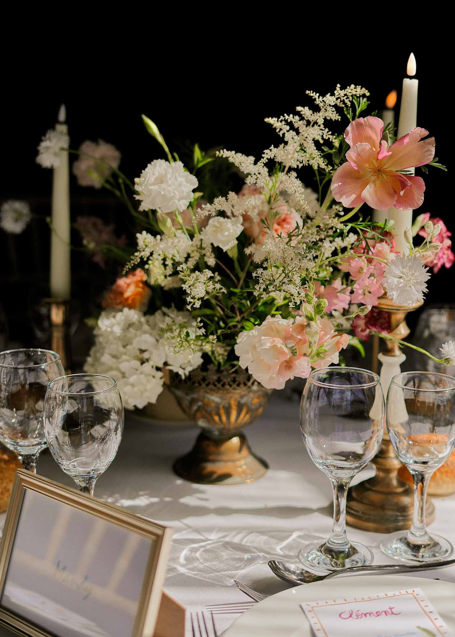 Elegant reception table setting with cream linens, brass urns with pink and ivory florals, and handwritten place cards