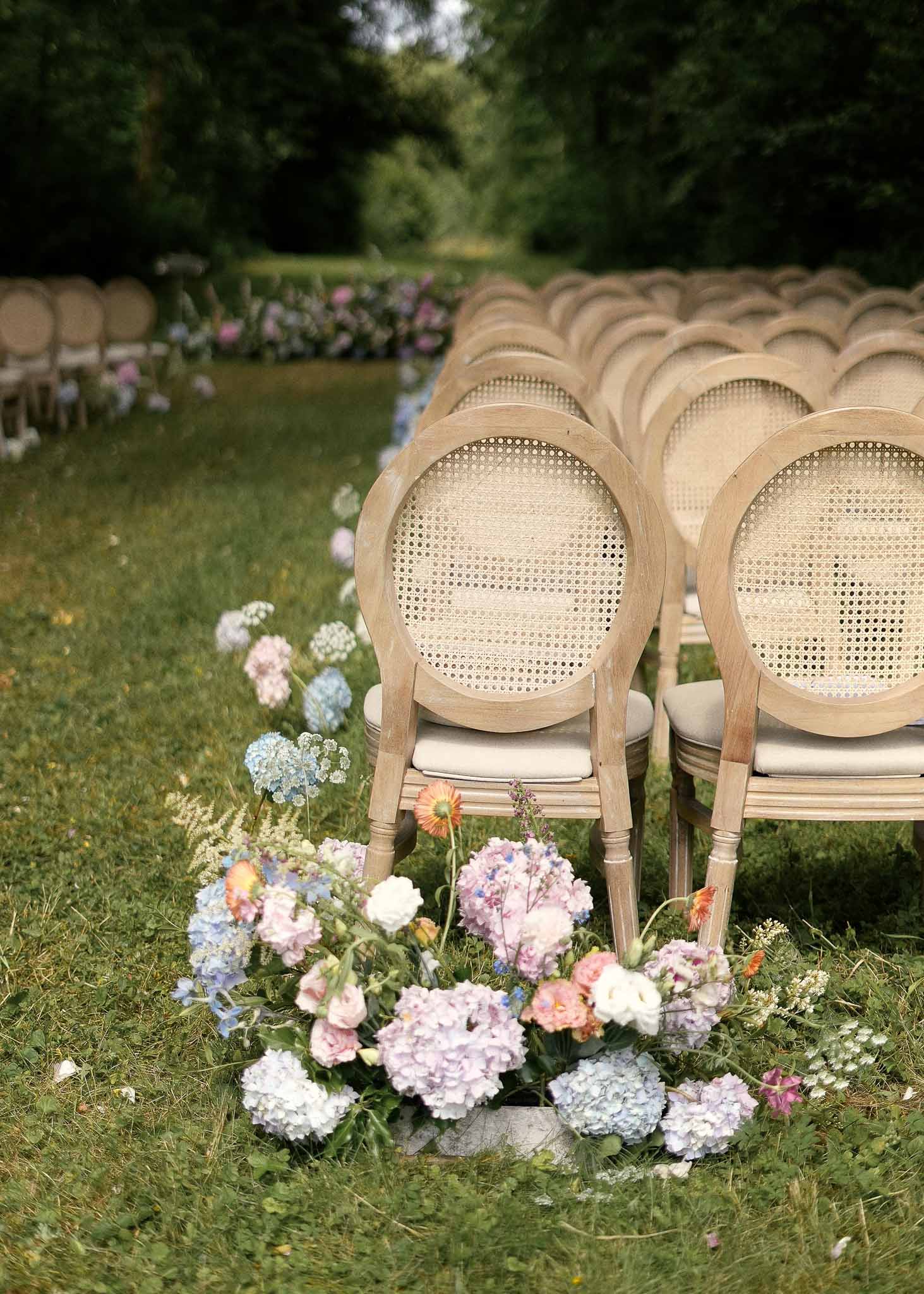 Ceremony seating with natural wood chairs and floral arrangements at outdoor garden wedding venue