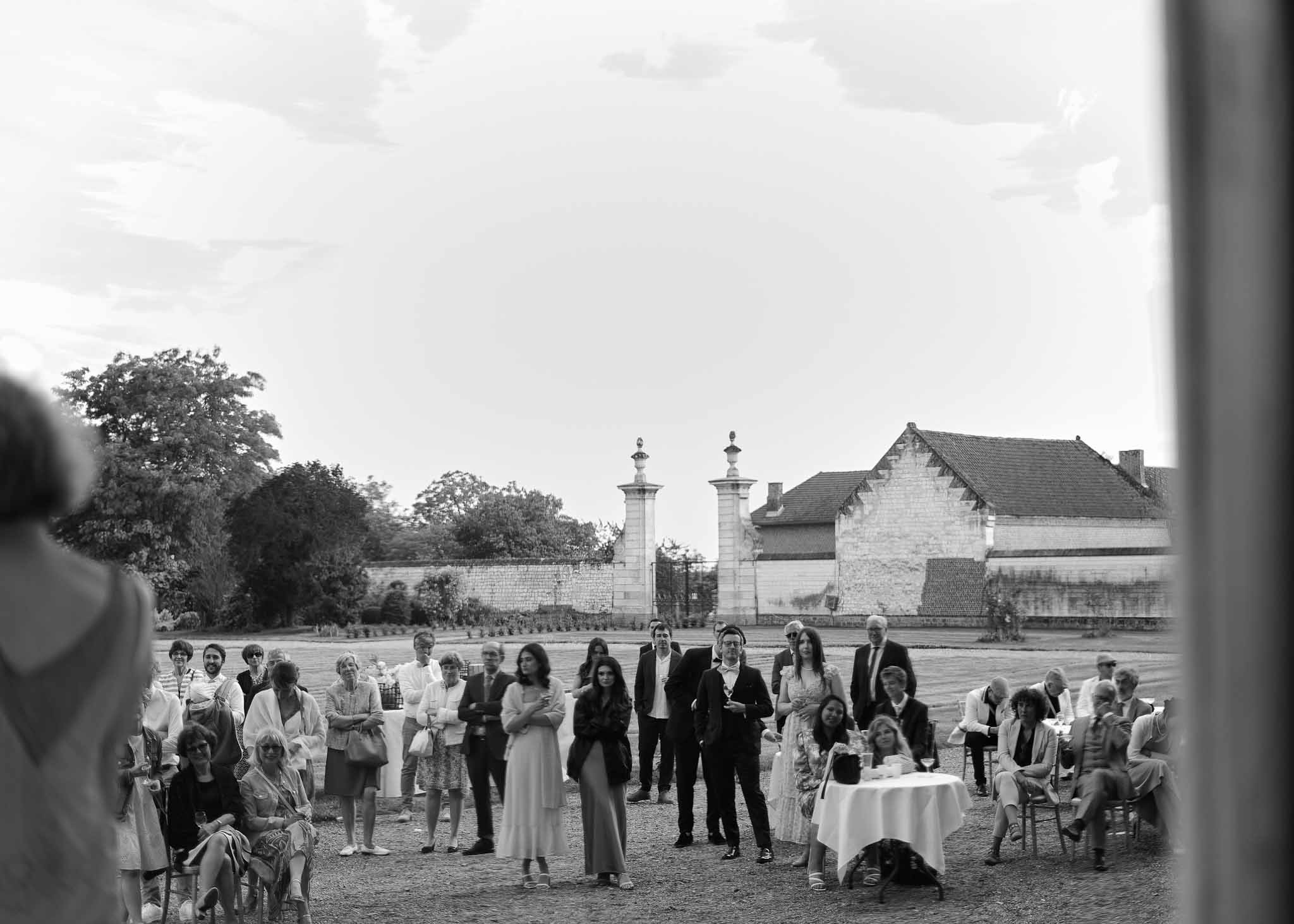 Outdoor wedding ceremony in courtyard of stone estate with twin gateposts and gathered guests