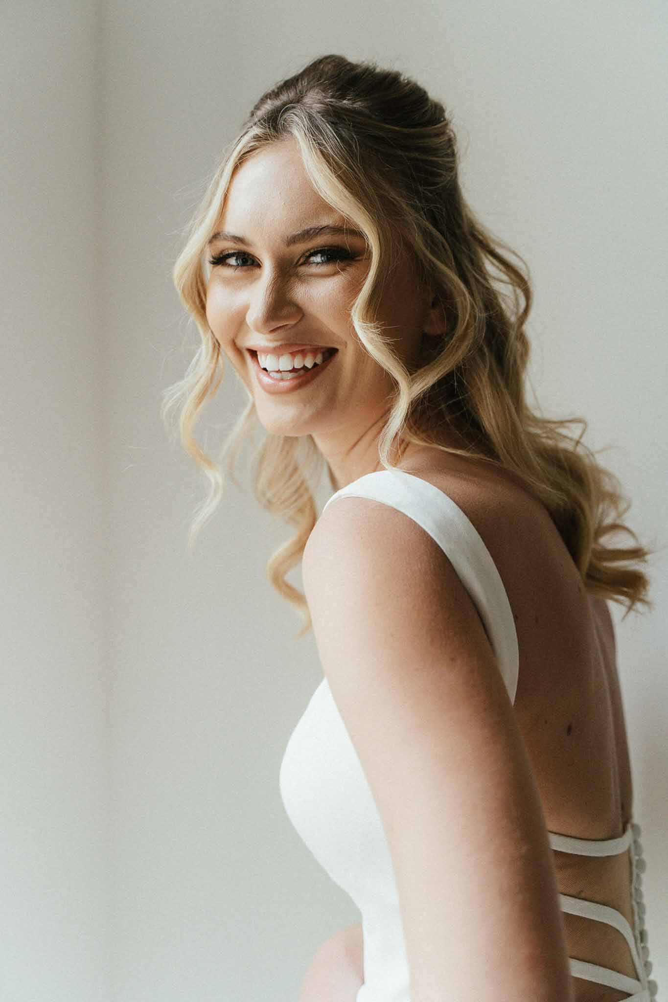 Bride smiling over shoulder showing low open back wedding dress during getting ready
