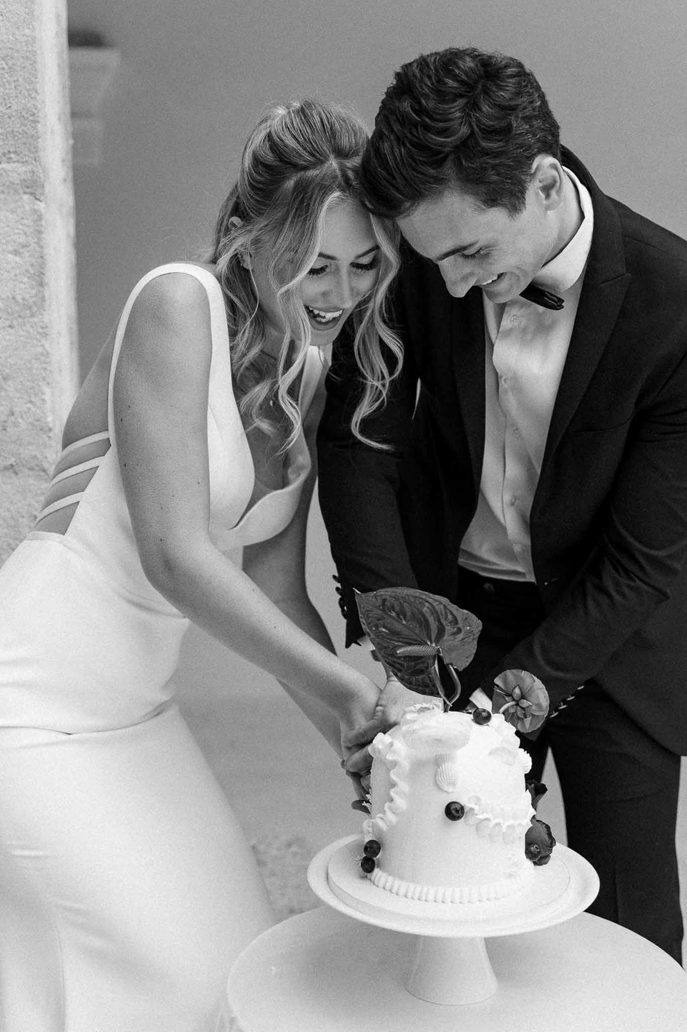 Black and white bride and groom laughing while cutting two-tier decorated cake