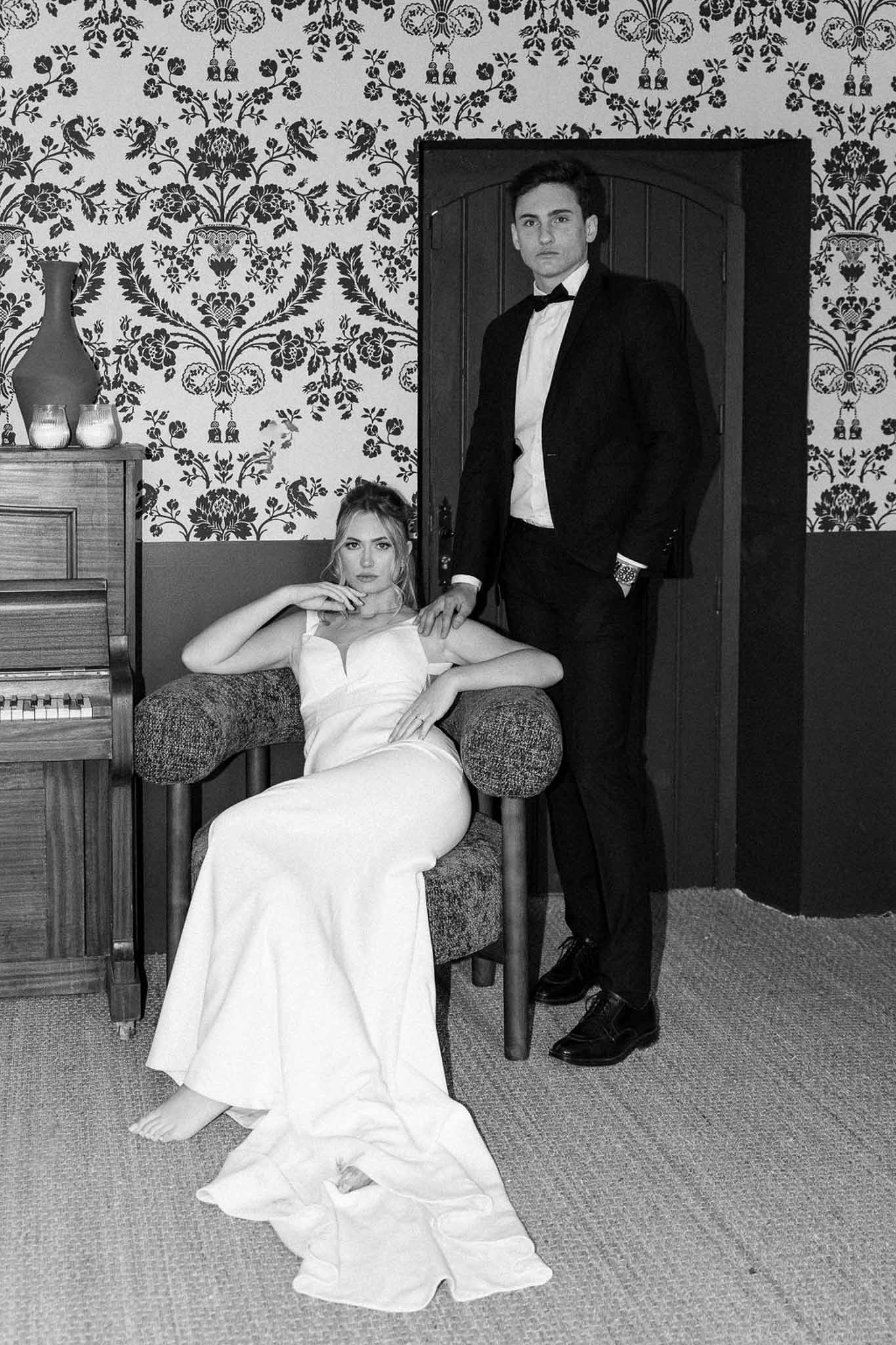Black and white portrait of bride and groom in elegant indoor setting with damask wallpaper
