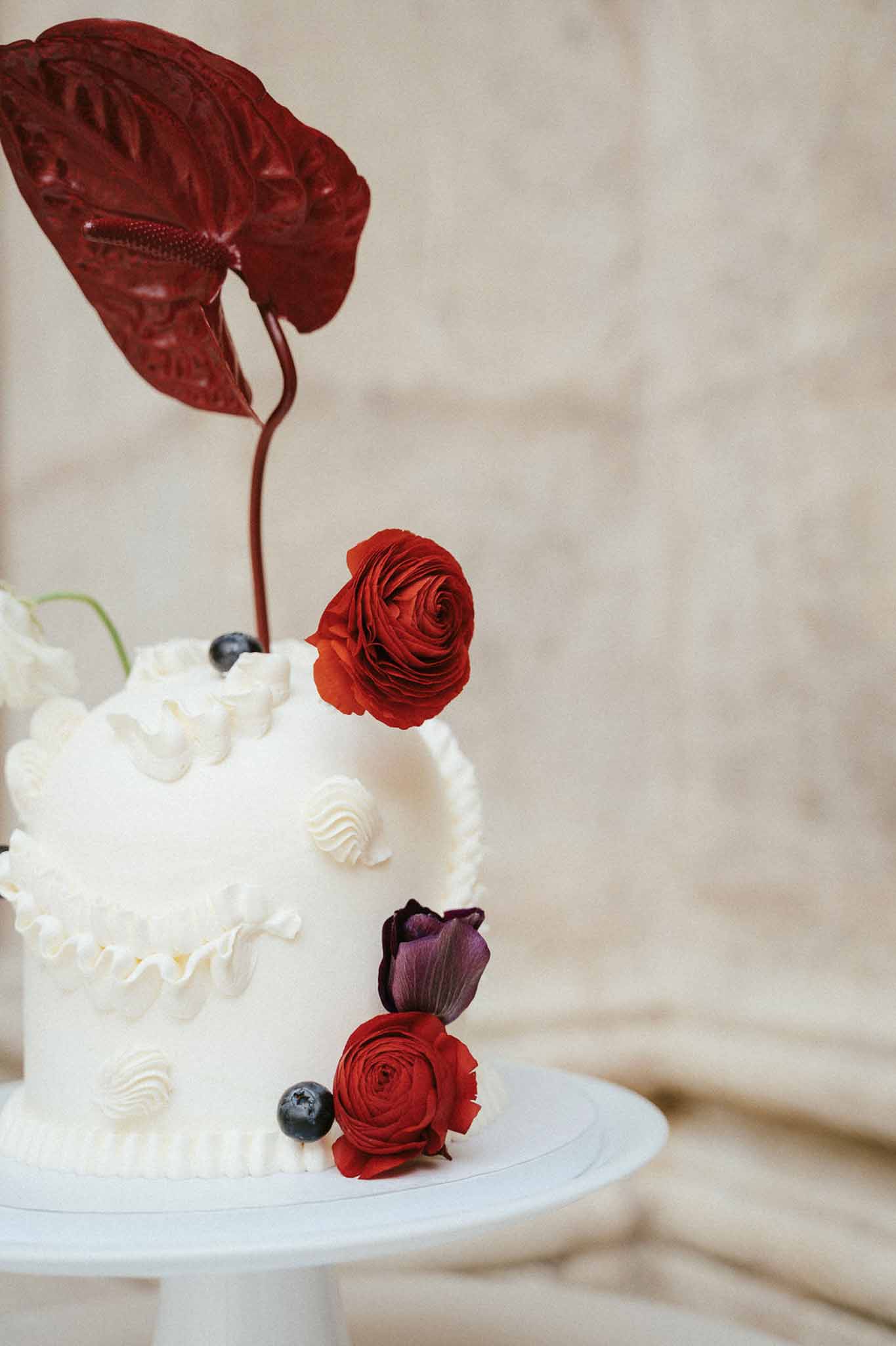 Two-tier wedding cake with ivory buttercream and red roses at elegant wedding venue