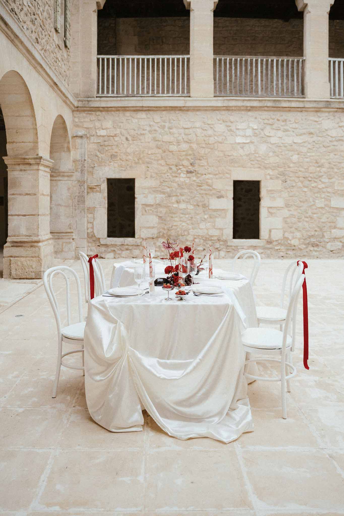 Historic stone courtyard with intimate reception table setup featuring red florals and limestone architecture
