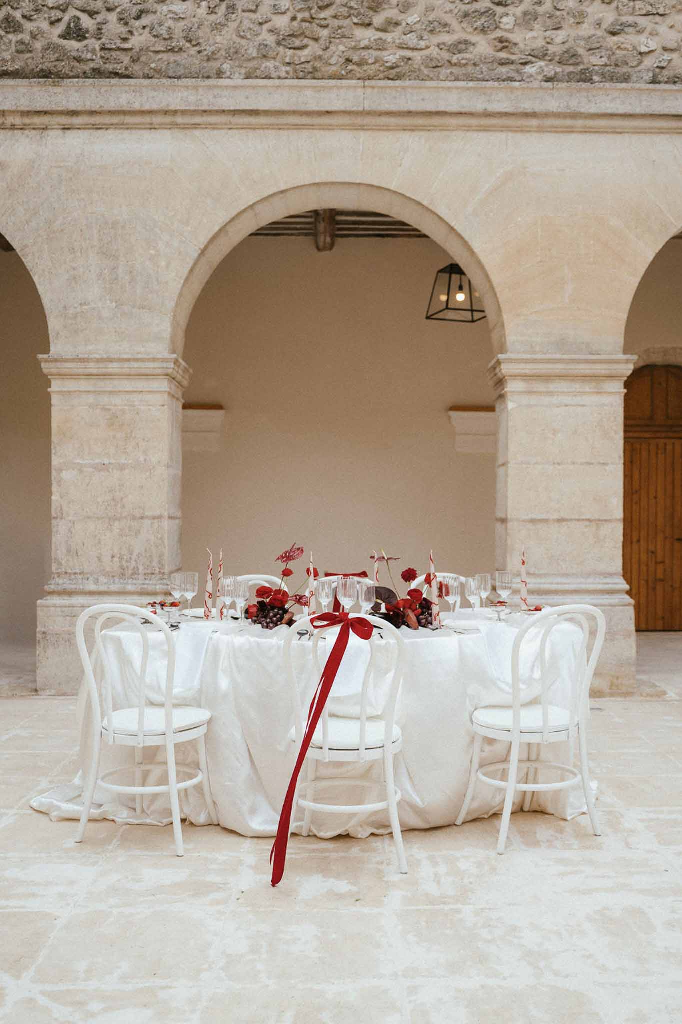Intimate sweetheart table with burgundy florals in stone courtyard with arched colonnades