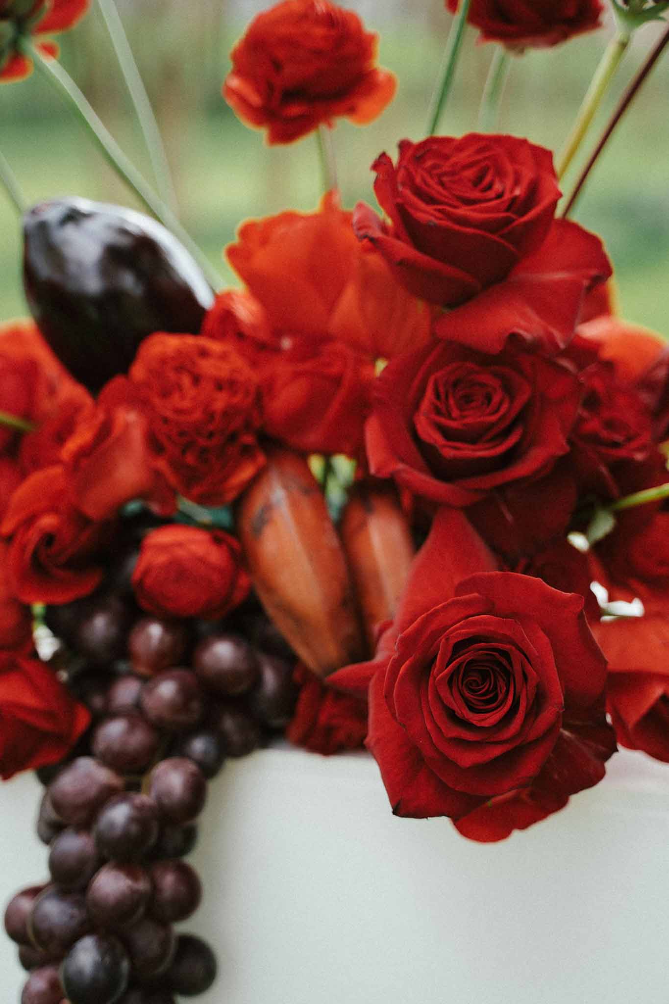 Deep red roses, grapes, and figs cascading over white wedding cake top tier in moody harvest-inspired arrangement