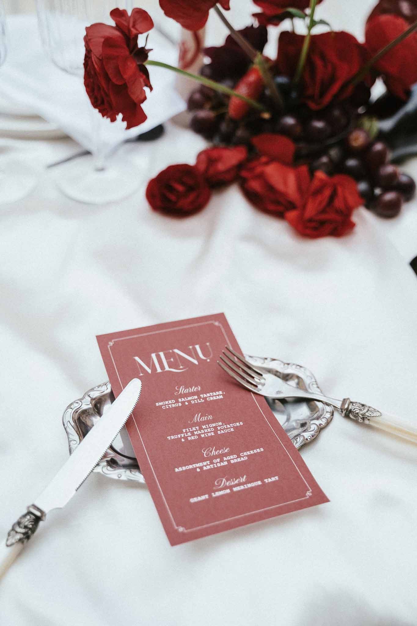 Formal table setting with dusty rose menu card and burgundy florals on silver charger plate