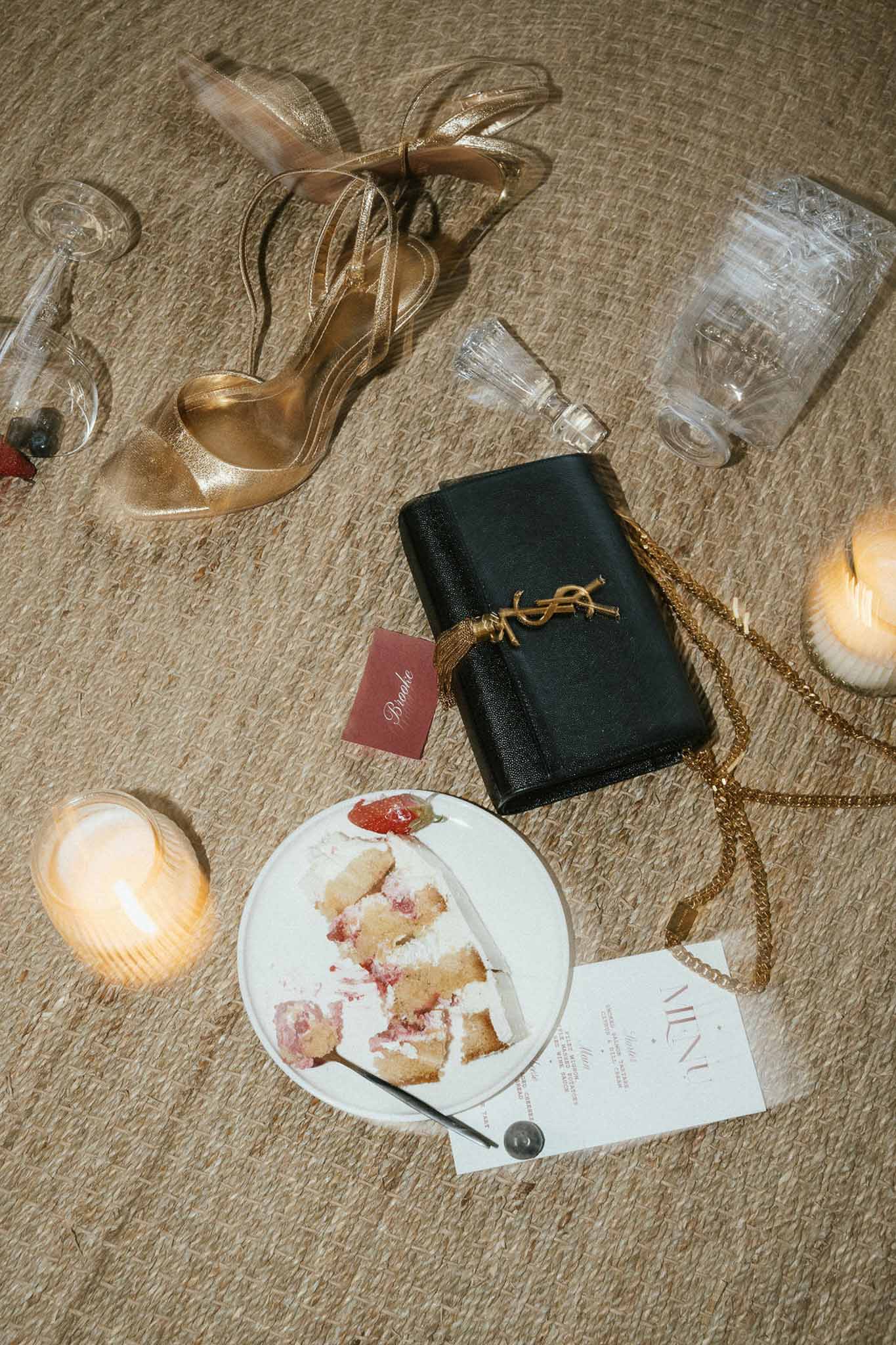 Wedding flat lay with gold shoes, black clutch, candles and cake on neutral linen fabric