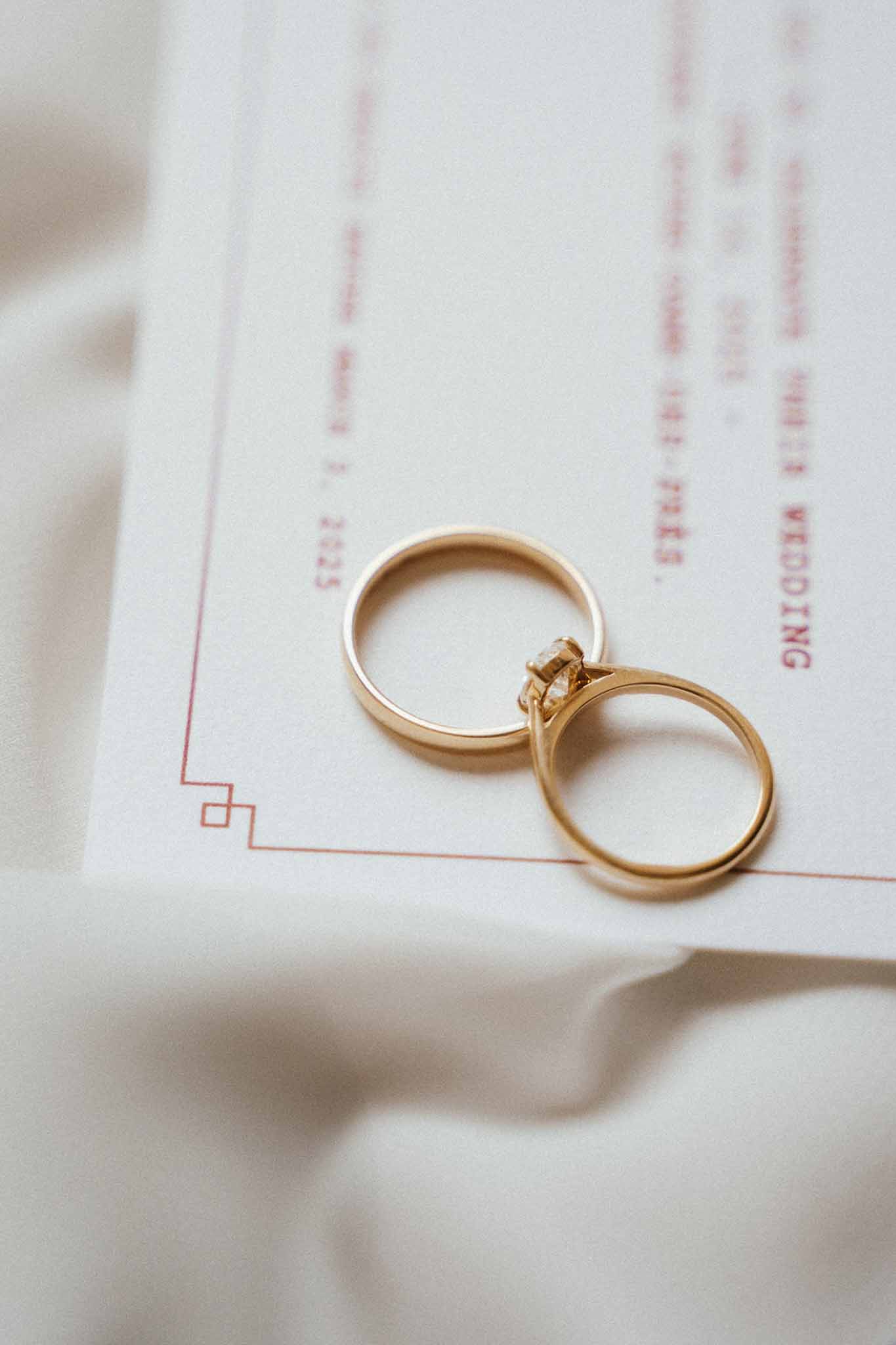 Two yellow gold wedding rings on white stationery card with red Art Deco border on ivory silk fabric
