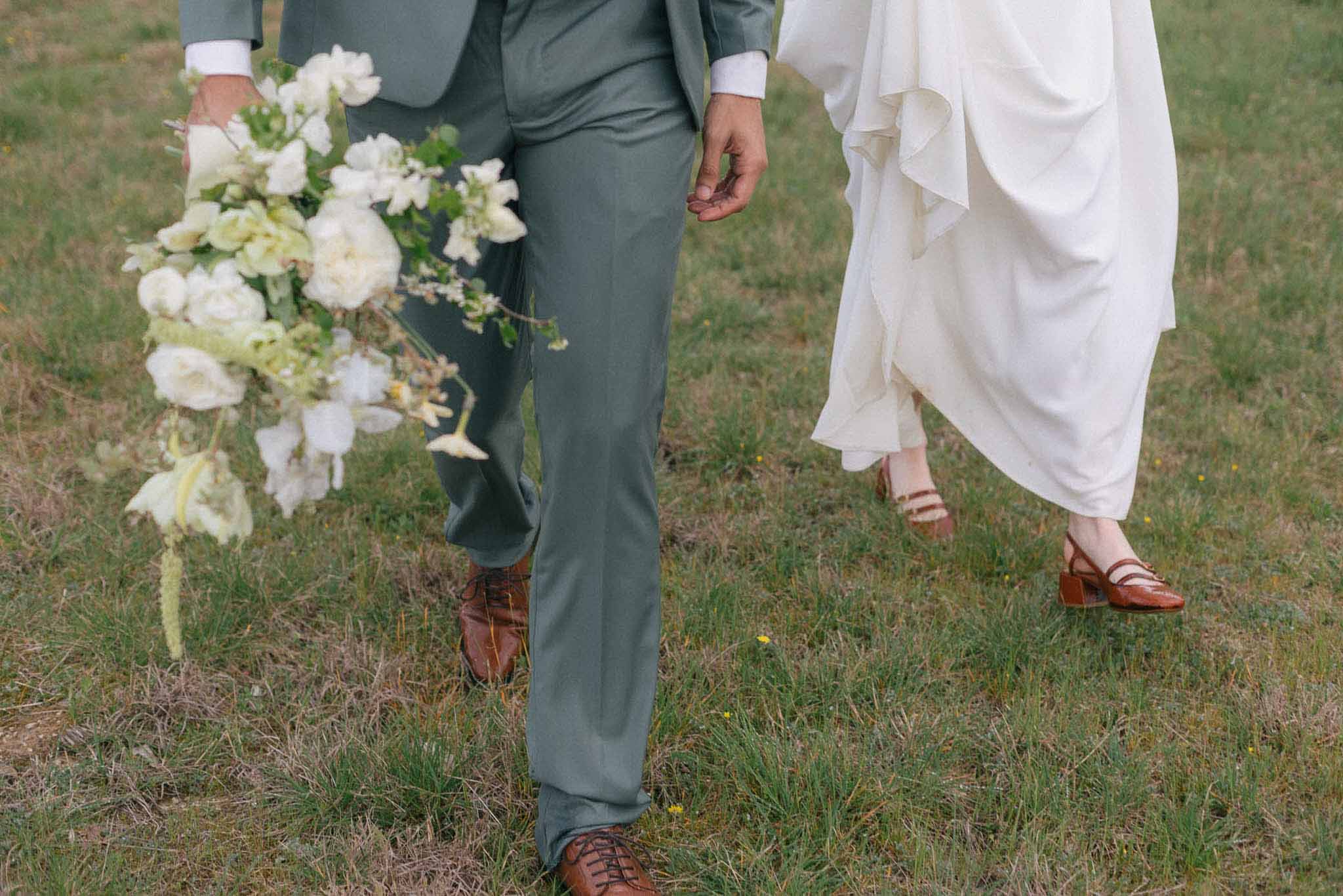 Bride and groom walking together in field showing wedding attire and bridal bouquet