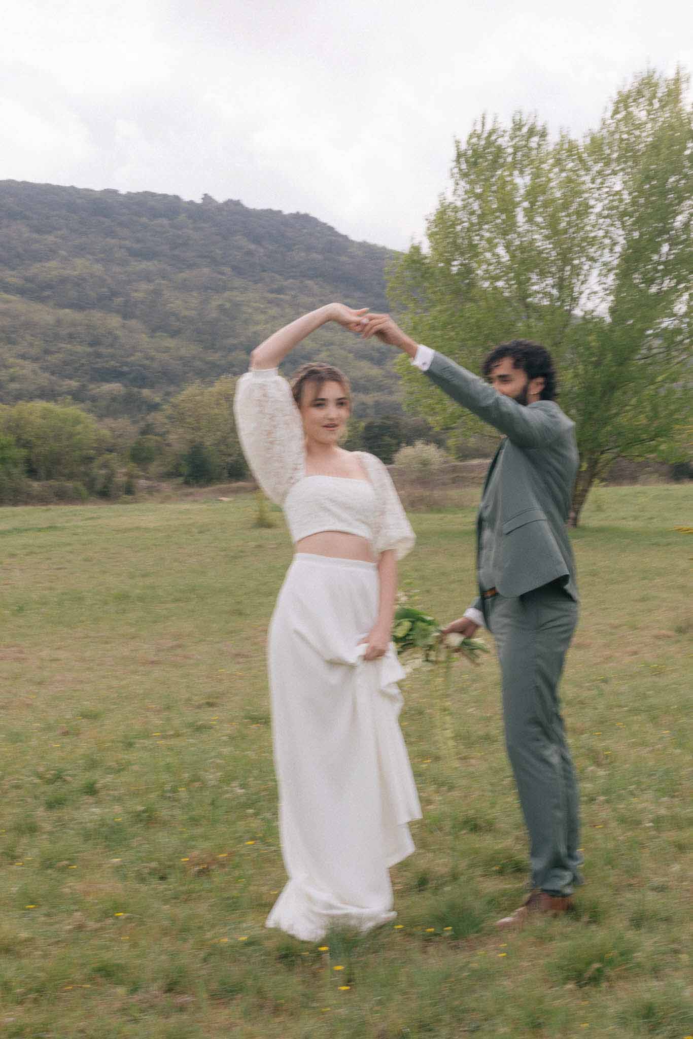 Bride and groom posing together in meadow with forested hills during portrait session
