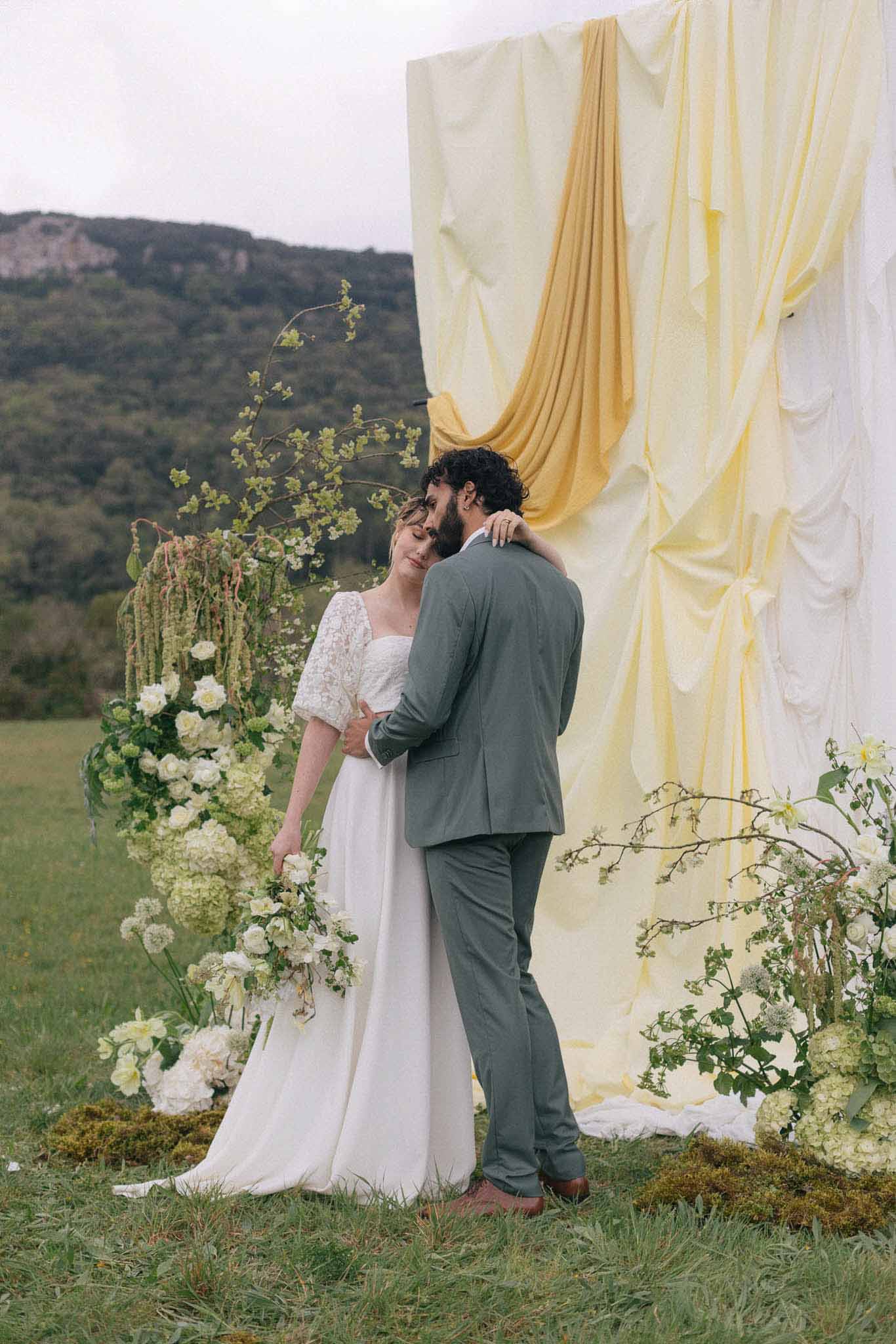 Bride and groom exchanging vows at outdoor ceremony with floral backdrop in rural valley setting
