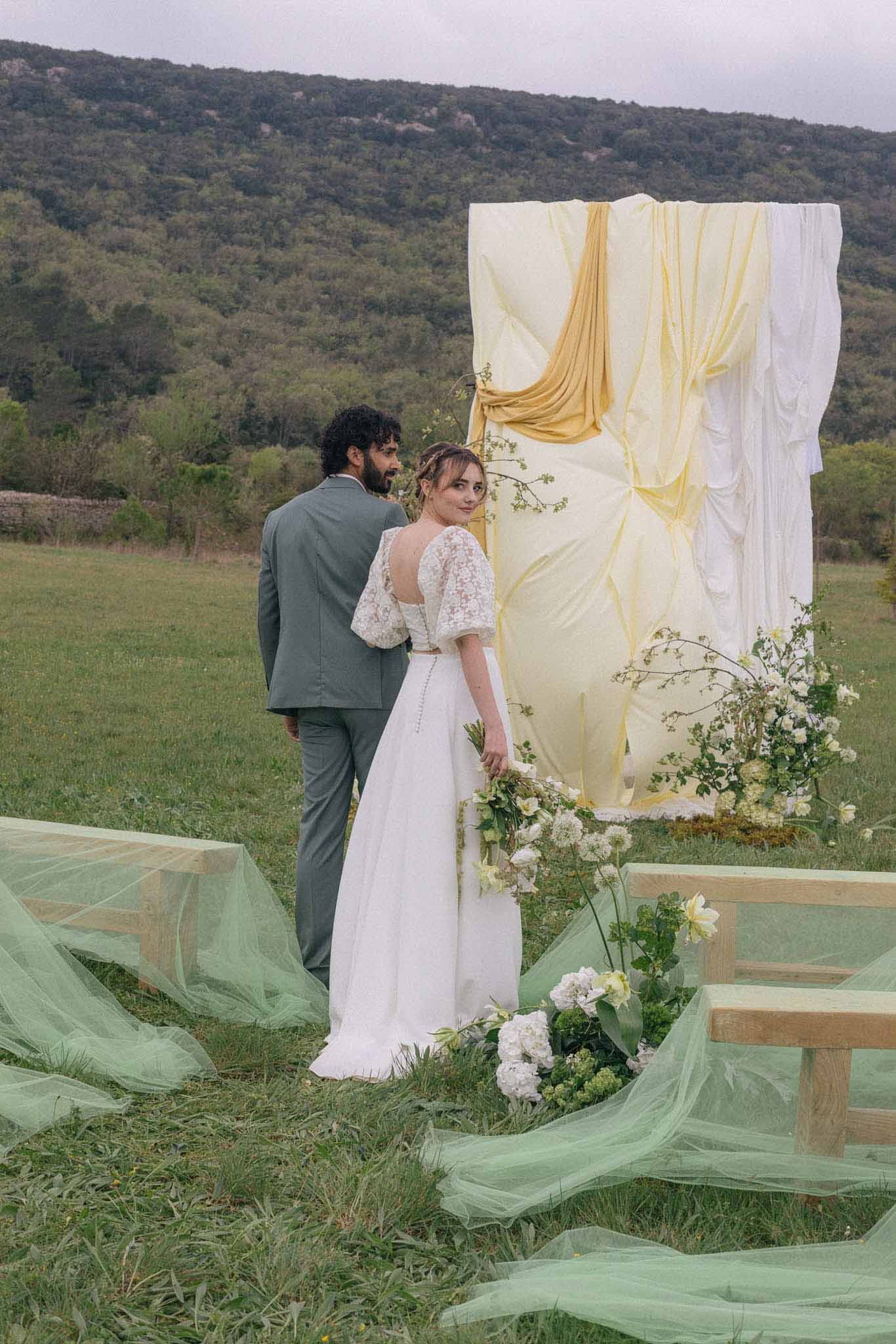 Bride and groom exchanging vows at outdoor hillside meadow ceremony with draped altar backdrop