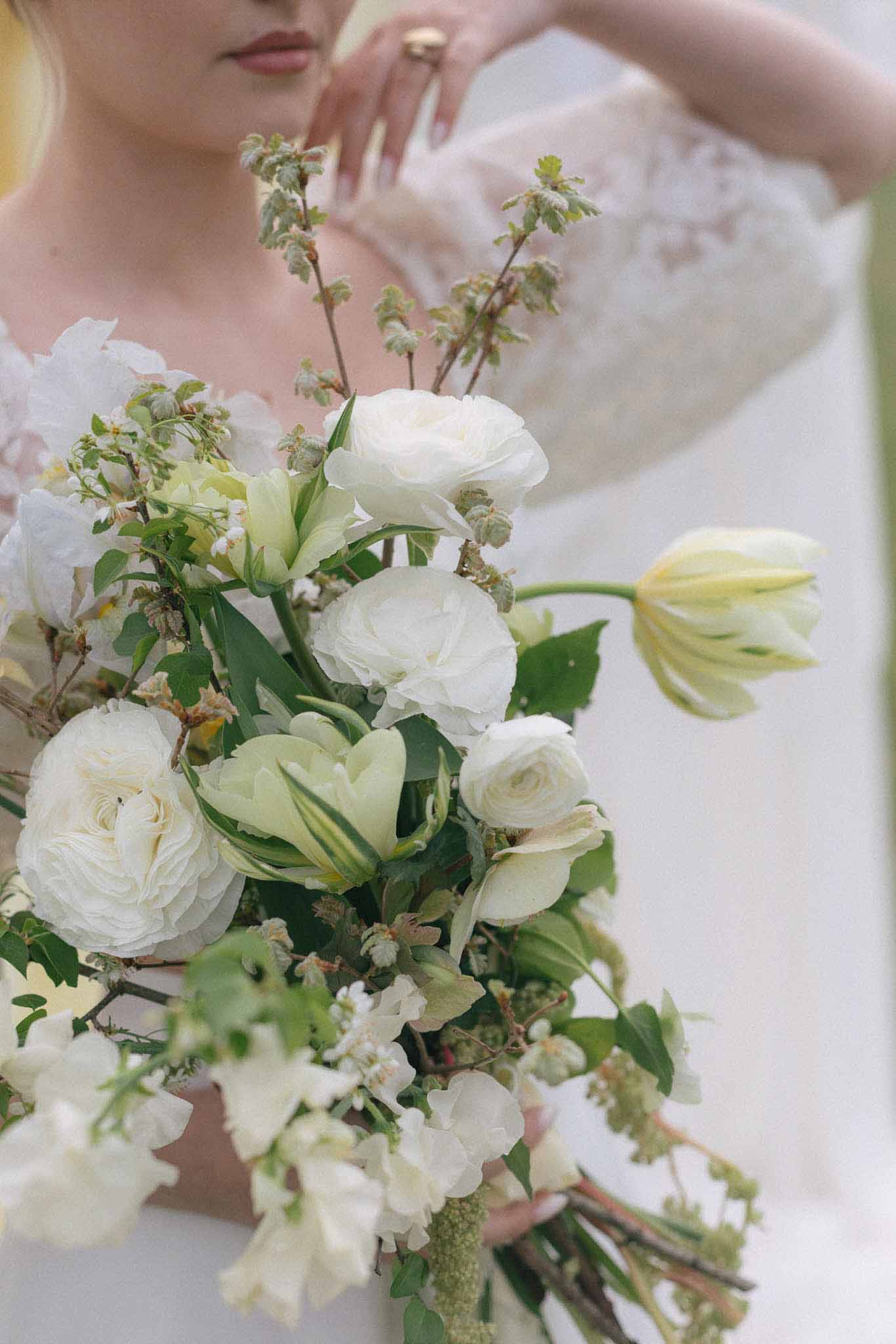 Bridal bouquet with ivory roses and white ranunculus held by bride in wedding dress