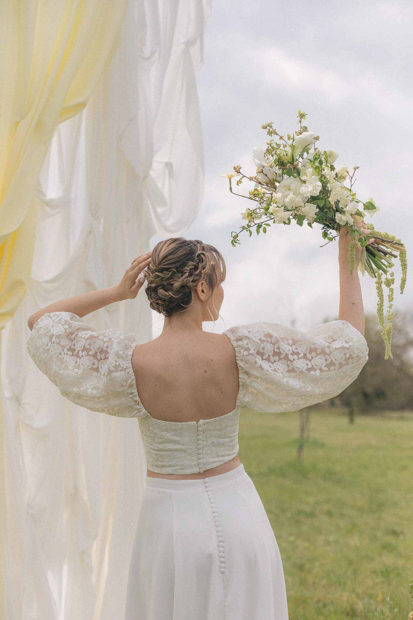 Bride holding bouquet adjusting hairstyle in outdoor wedding portrait