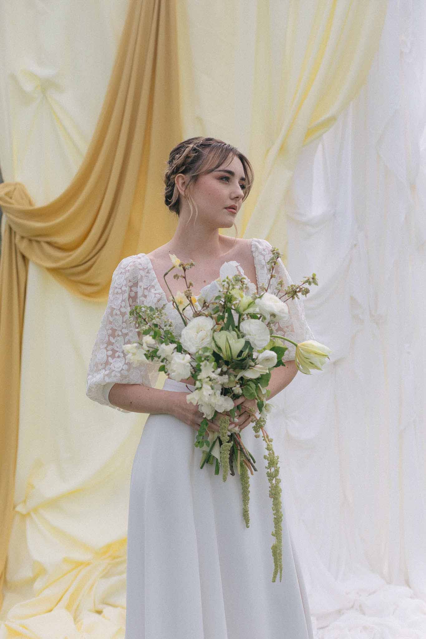 Bride holding white rose bouquet against cream fabric backdrop in portrait session