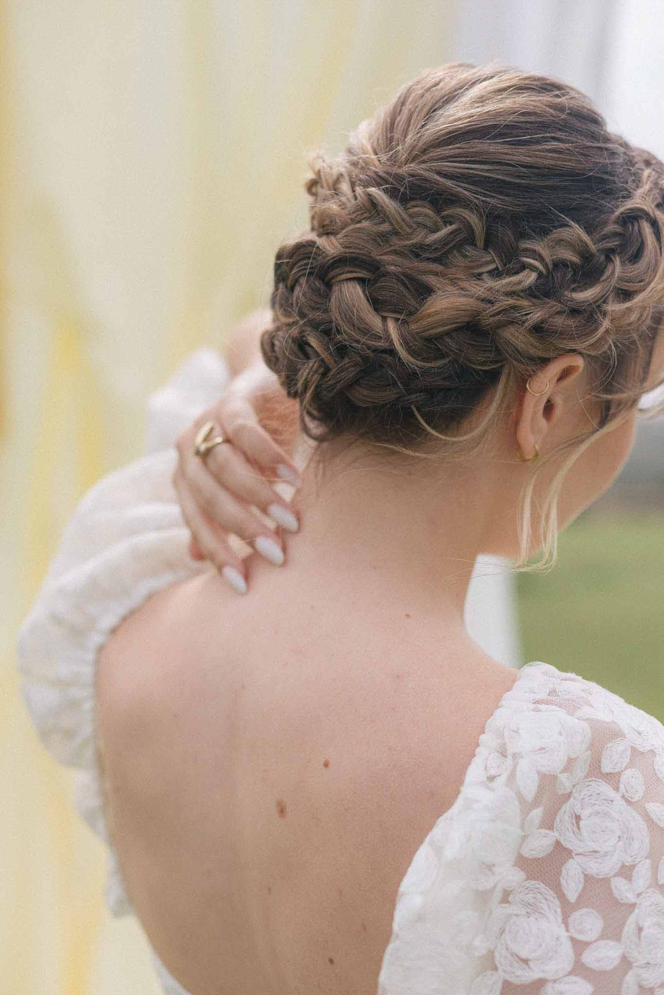 Close-up of bride's intricate updo hairstyle and lace gown details from behind