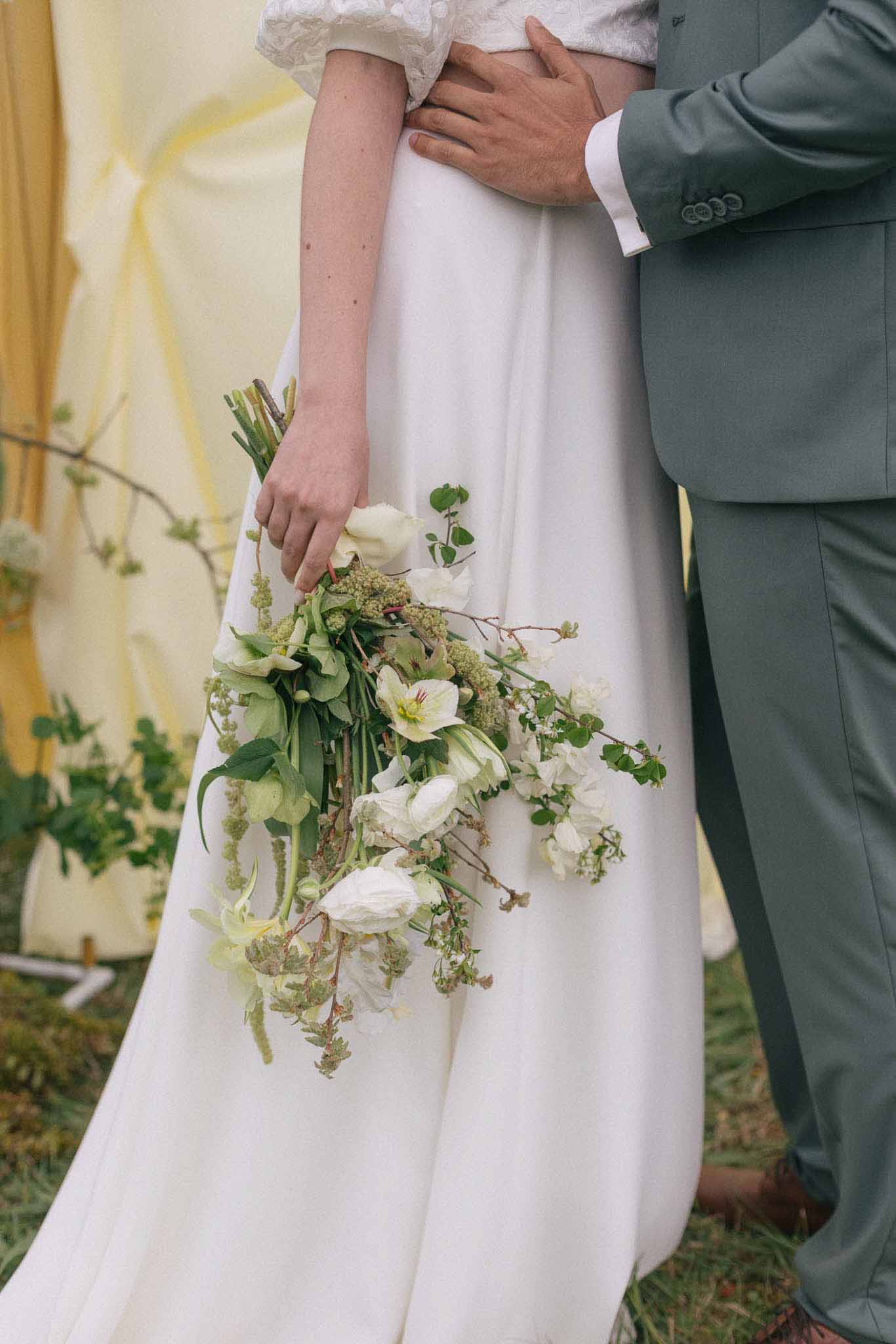 Bride and groom during outdoor ceremony with cascading bouquet and sage green suit