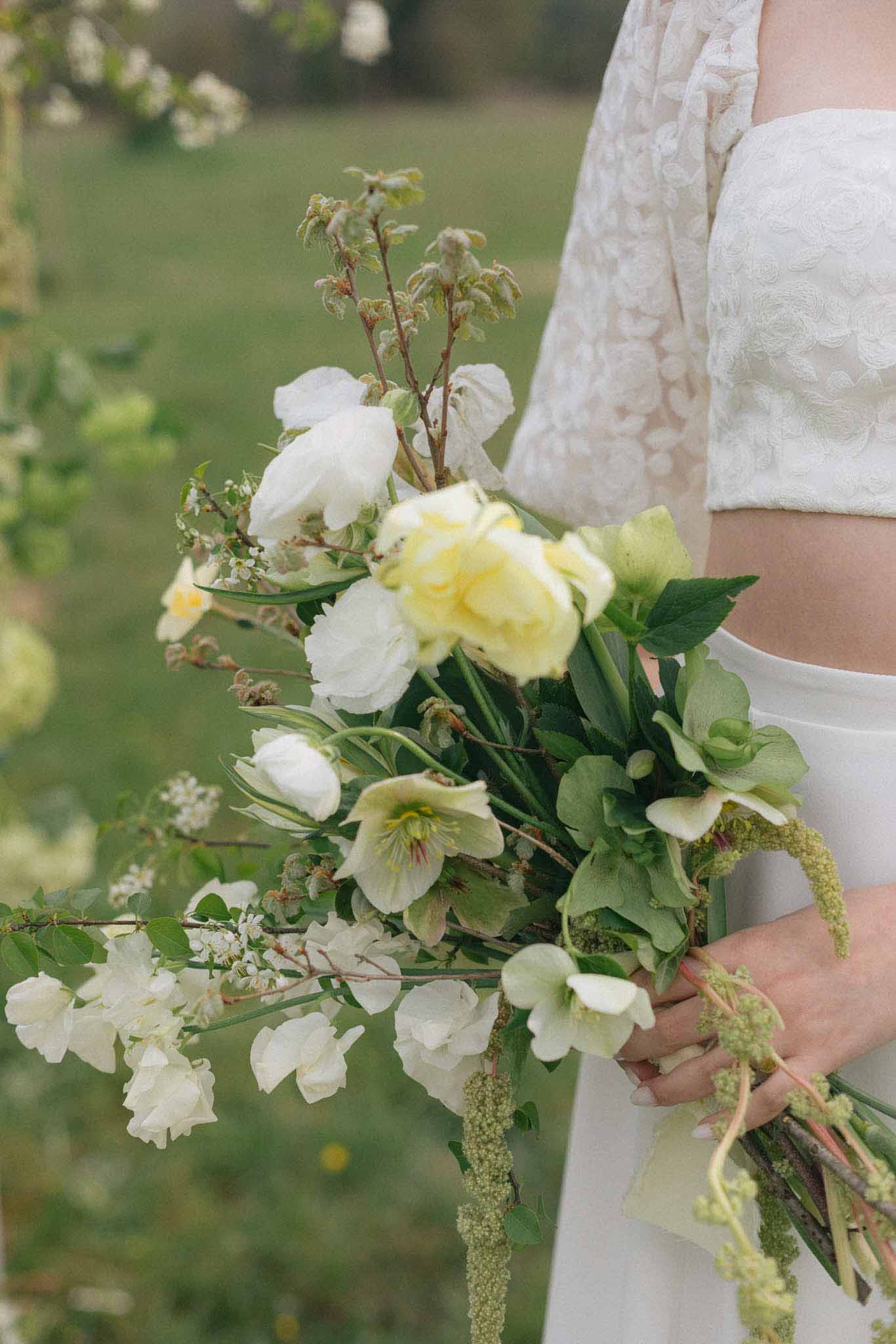 Bride holding garden-style bouquet with white sweet peas and cream hellebores in outdoor garden setting