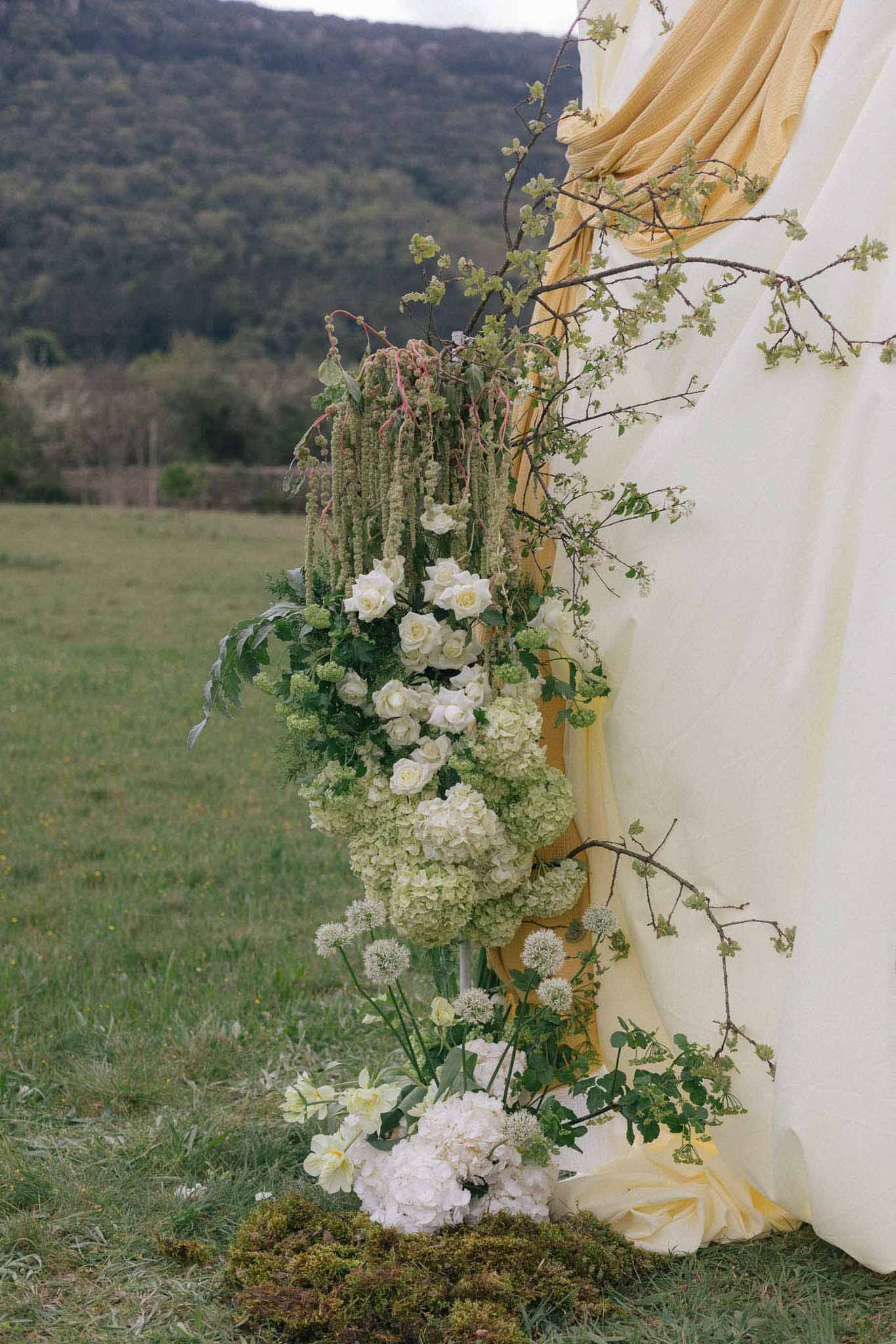Close-up floral ceremony installation with ivory roses and burgundy amaranthus at outdoor countryside venue