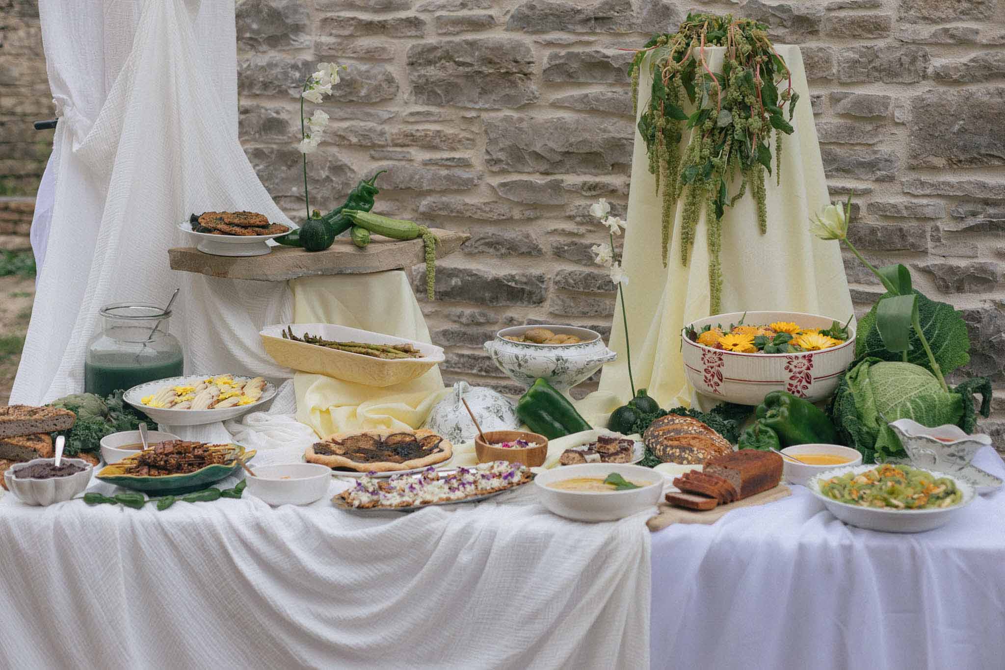 Rustic wedding food display with white linens and greenery against stone wall at outdoor reception