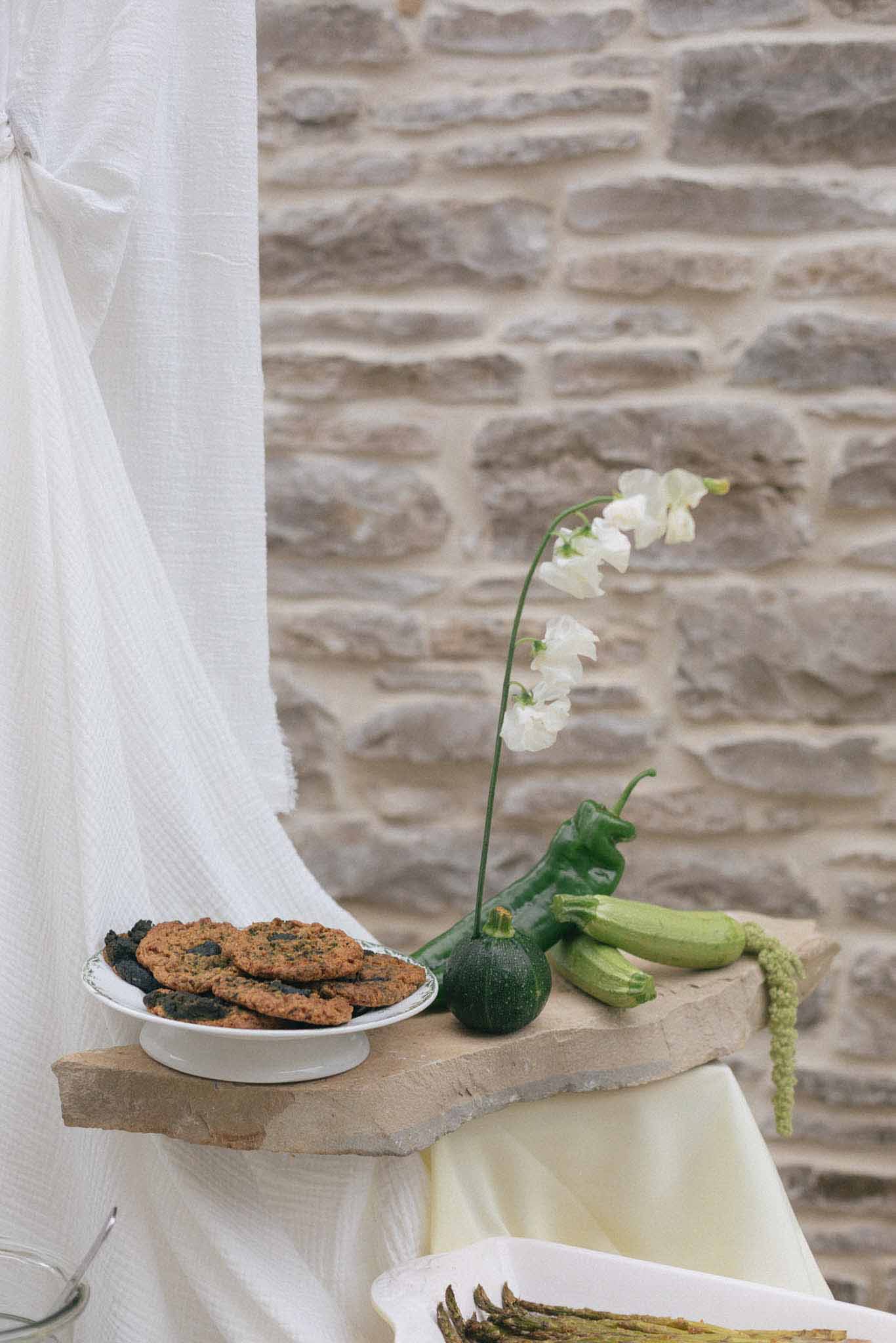 Rustic wooden shelf with wedding reception cookies and fresh vegetables against stone wall