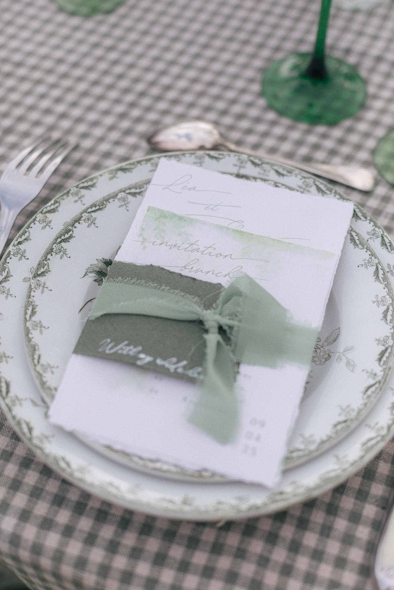 Wedding place setting with botanical plate and sage ribbon menu card on gray linen tablecloth