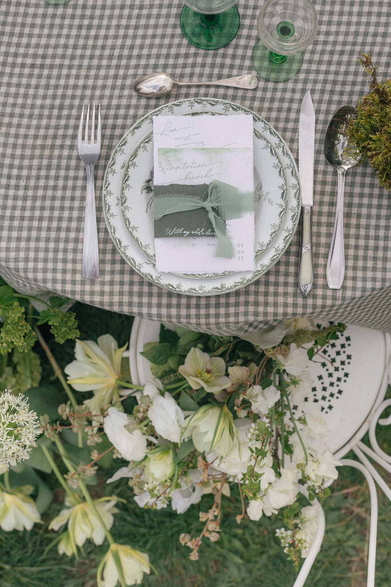 Overhead view of elegant table setting with sage green accents and white floral centerpiece at garden reception