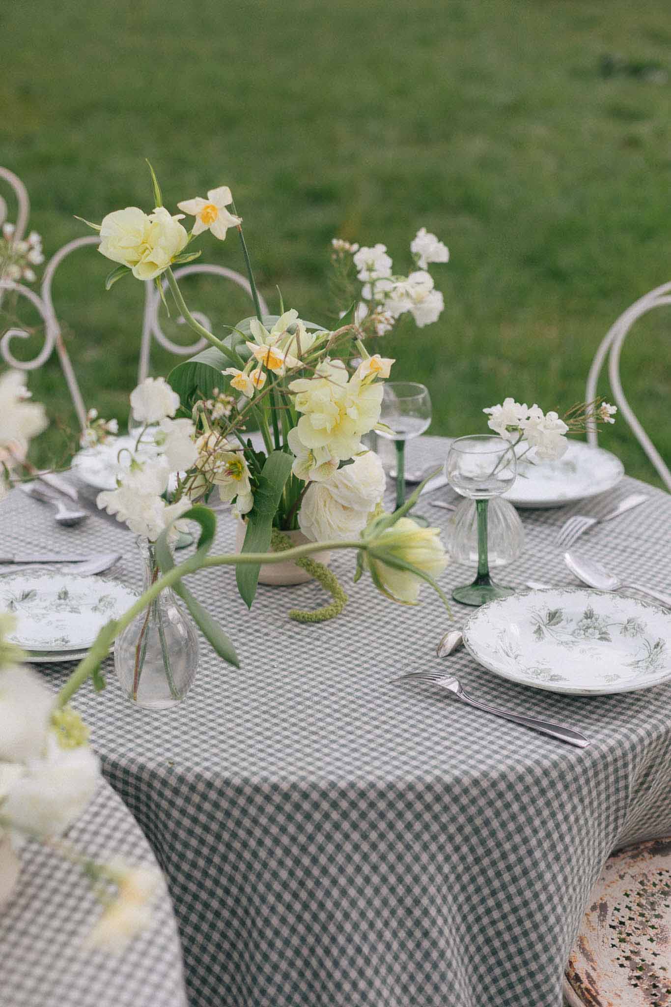 Spring table setting with sage gingham linen and daffodil centerpiece at outdoor garden reception