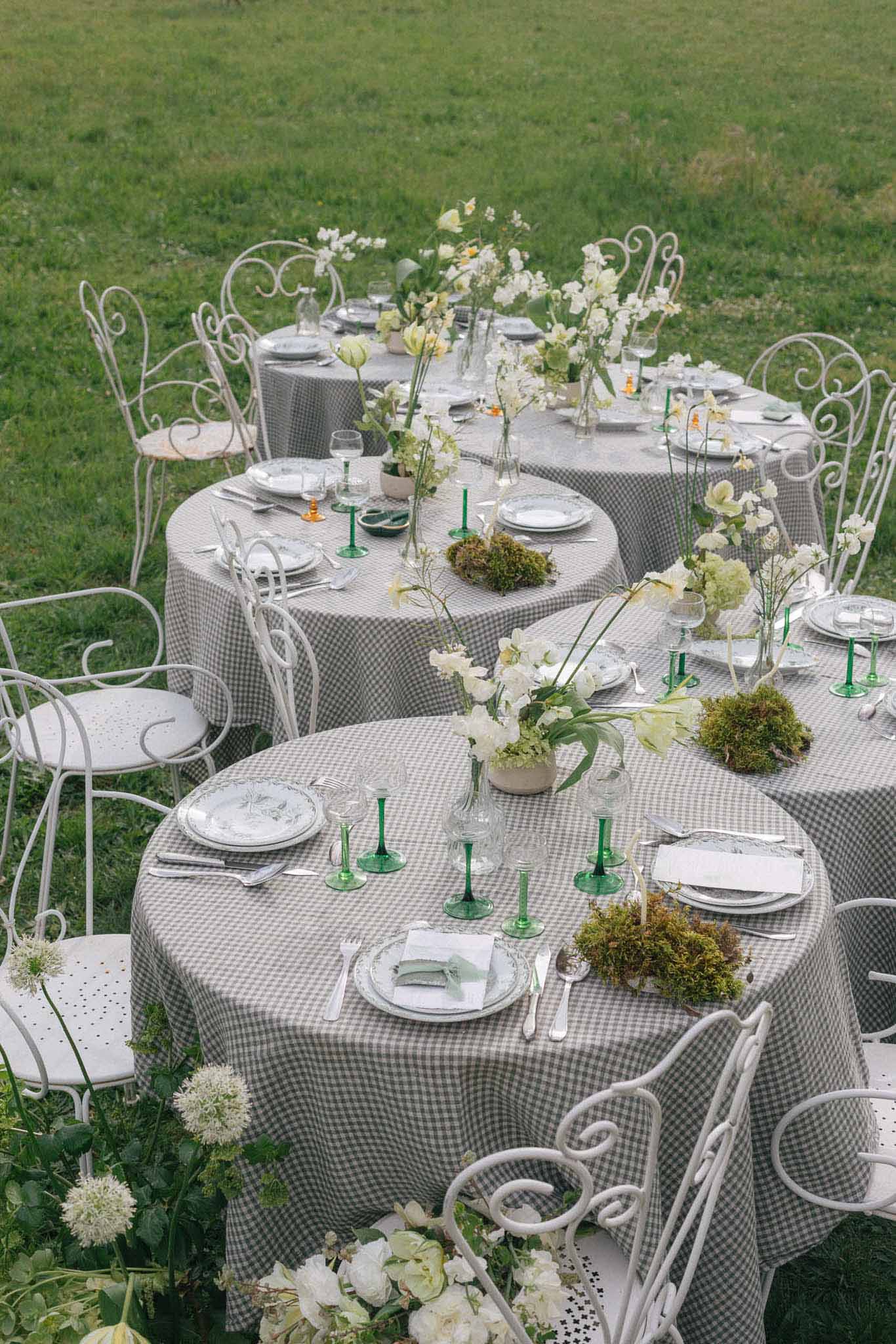 Aerial view of outdoor reception table settings with gingham linens and white floral centerpieces on green lawn