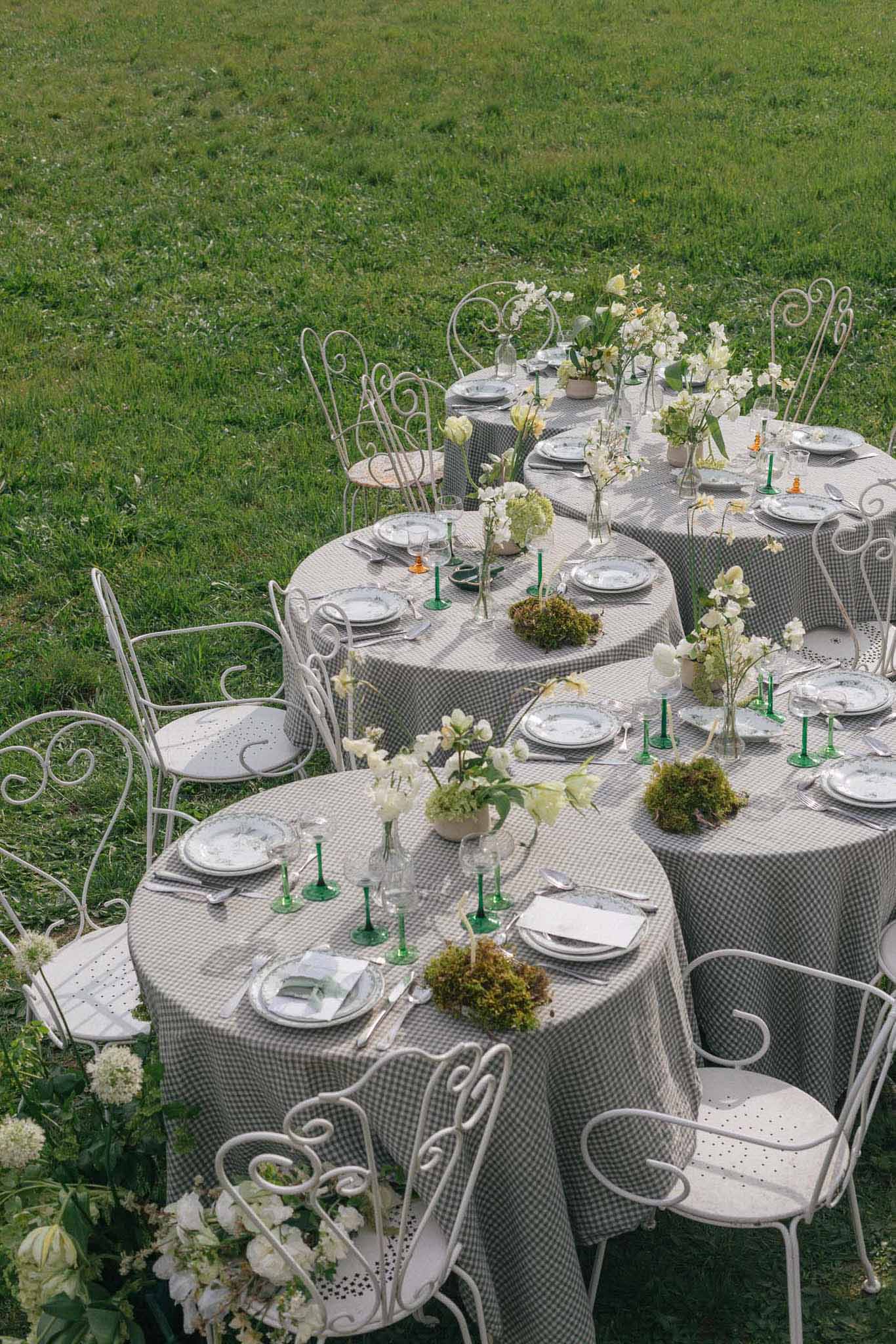 Outdoor reception table settings with gingham linens and white floral centerpieces on manicured lawn