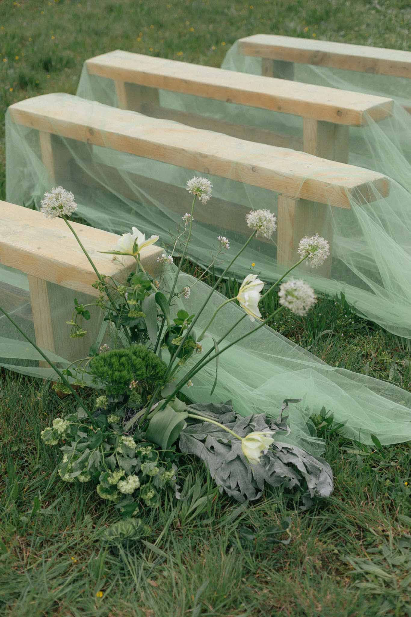 Wedding ceremony seating with sage tulle draping and wildflower bouquet at outdoor garden venue