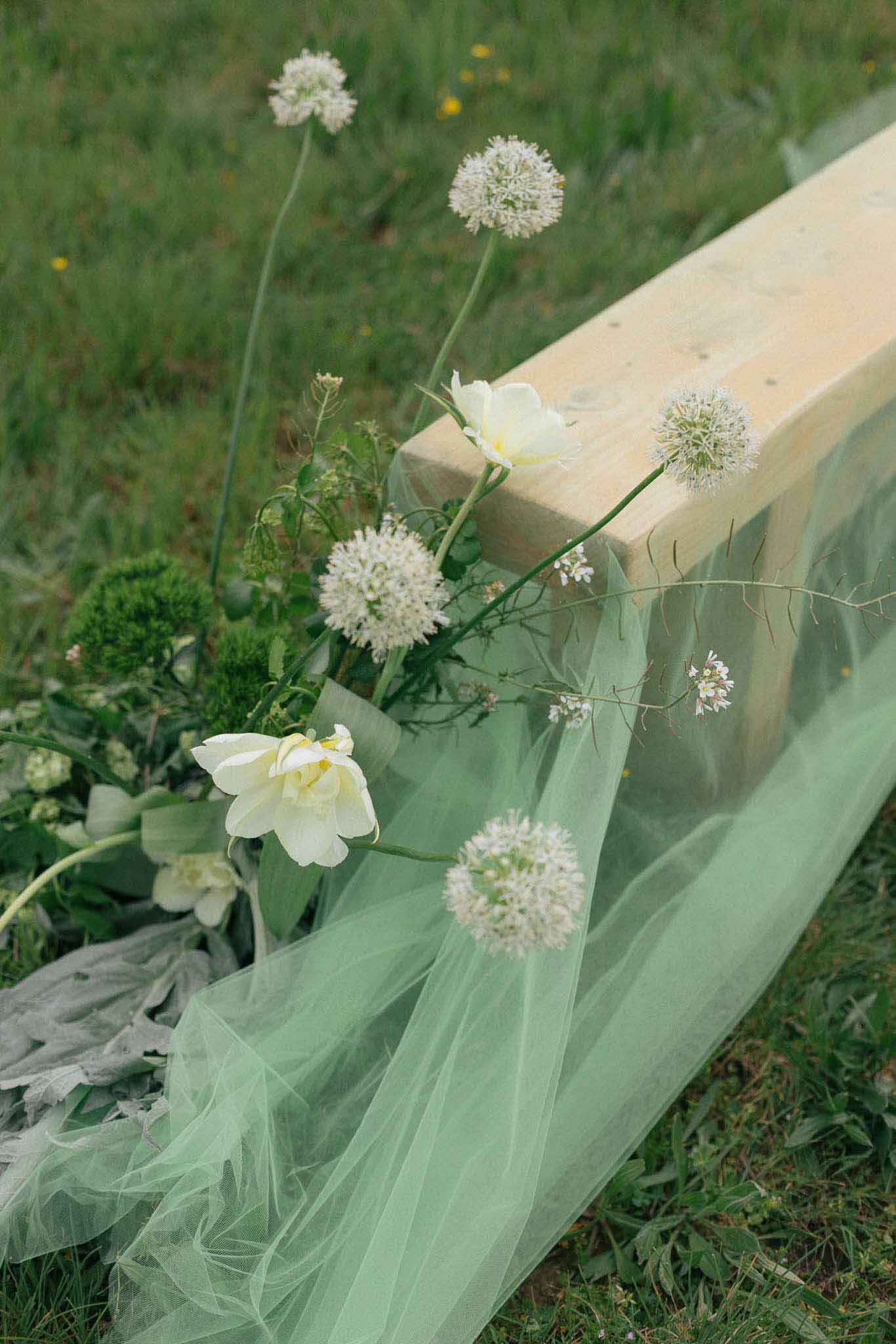 Cream tulle and white flowers draped over wooden beam at outdoor garden wedding ceremony