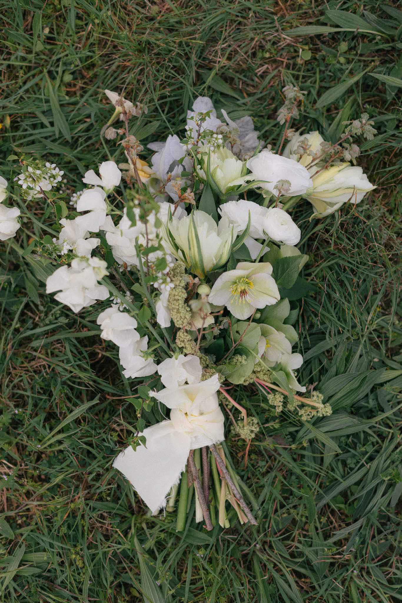 Bridal bouquet with ivory hellebores and sage greenery laid on grass