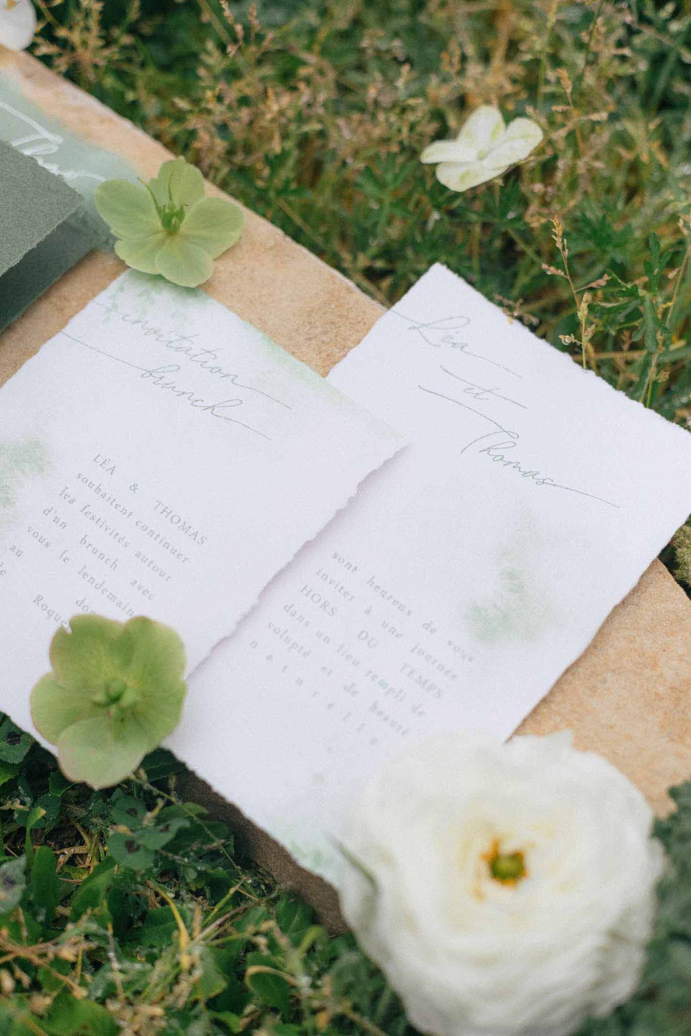 Wedding invitation flat lay with cream stationery, hydrangeas and ranunculus on natural linen surface