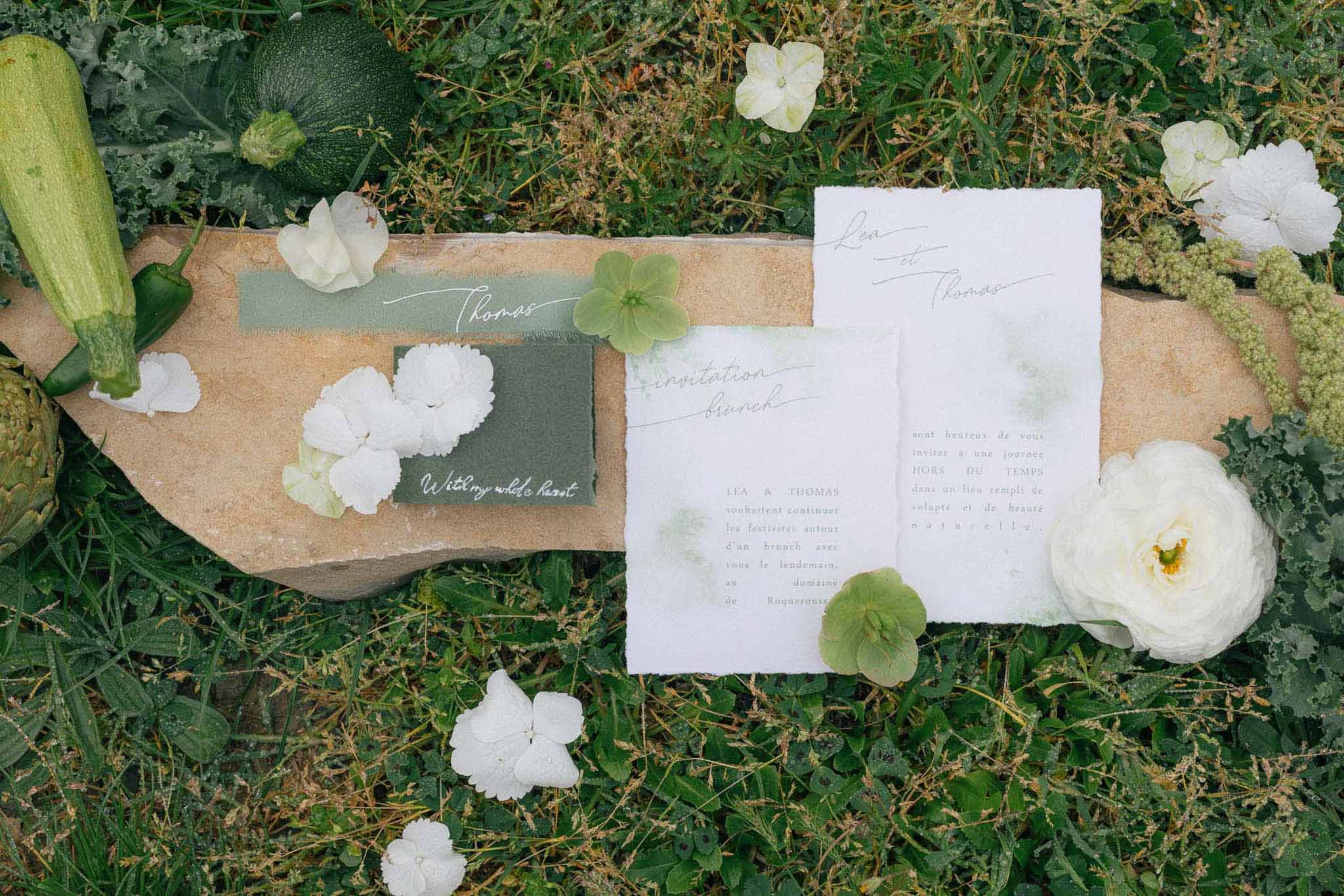 Wedding stationery flat lay with sage green cards and white peonies on natural textures