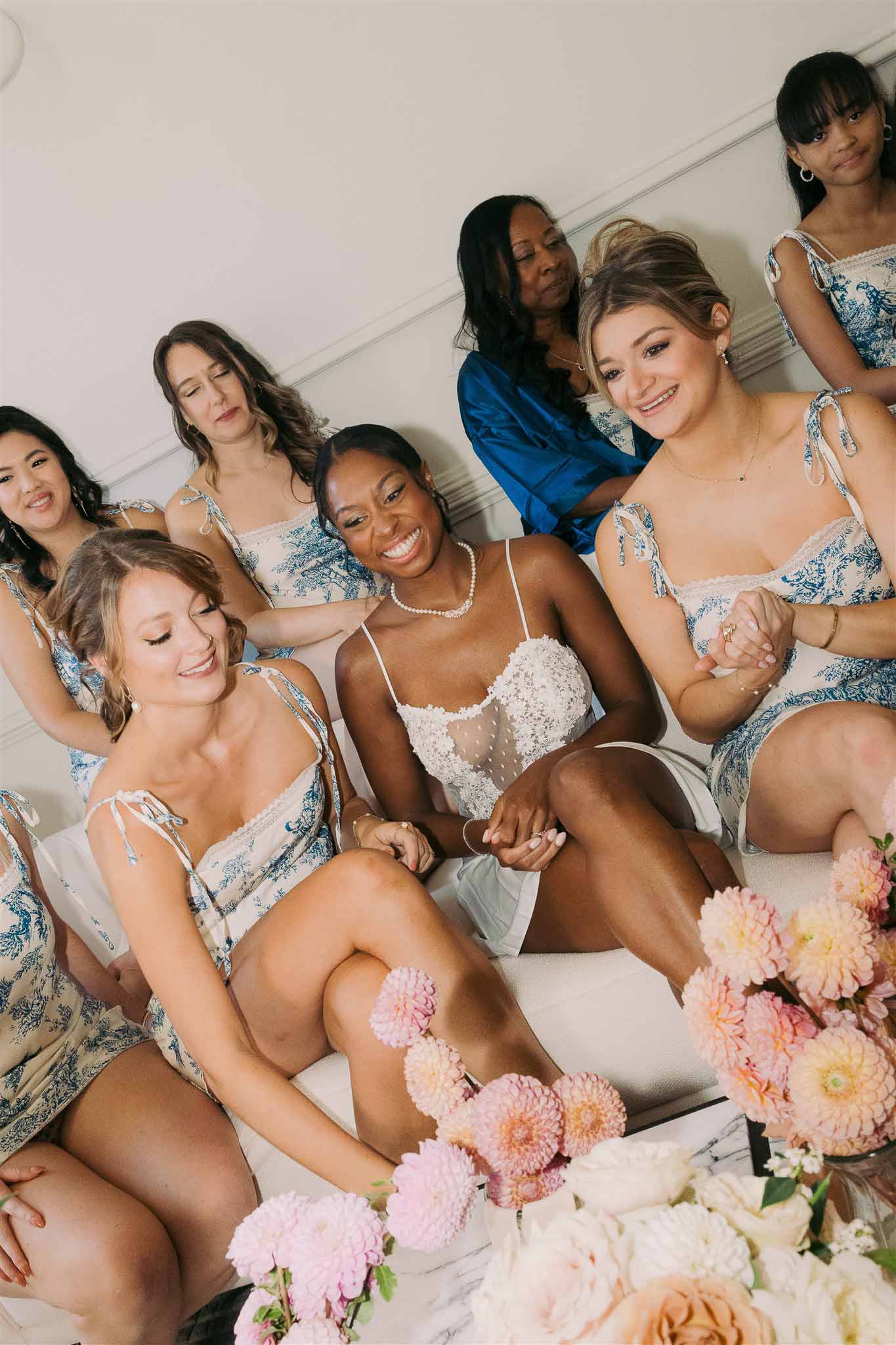 Bride and bridesmaids in blue patterned dresses with pink dahlias during getting ready moment indoors