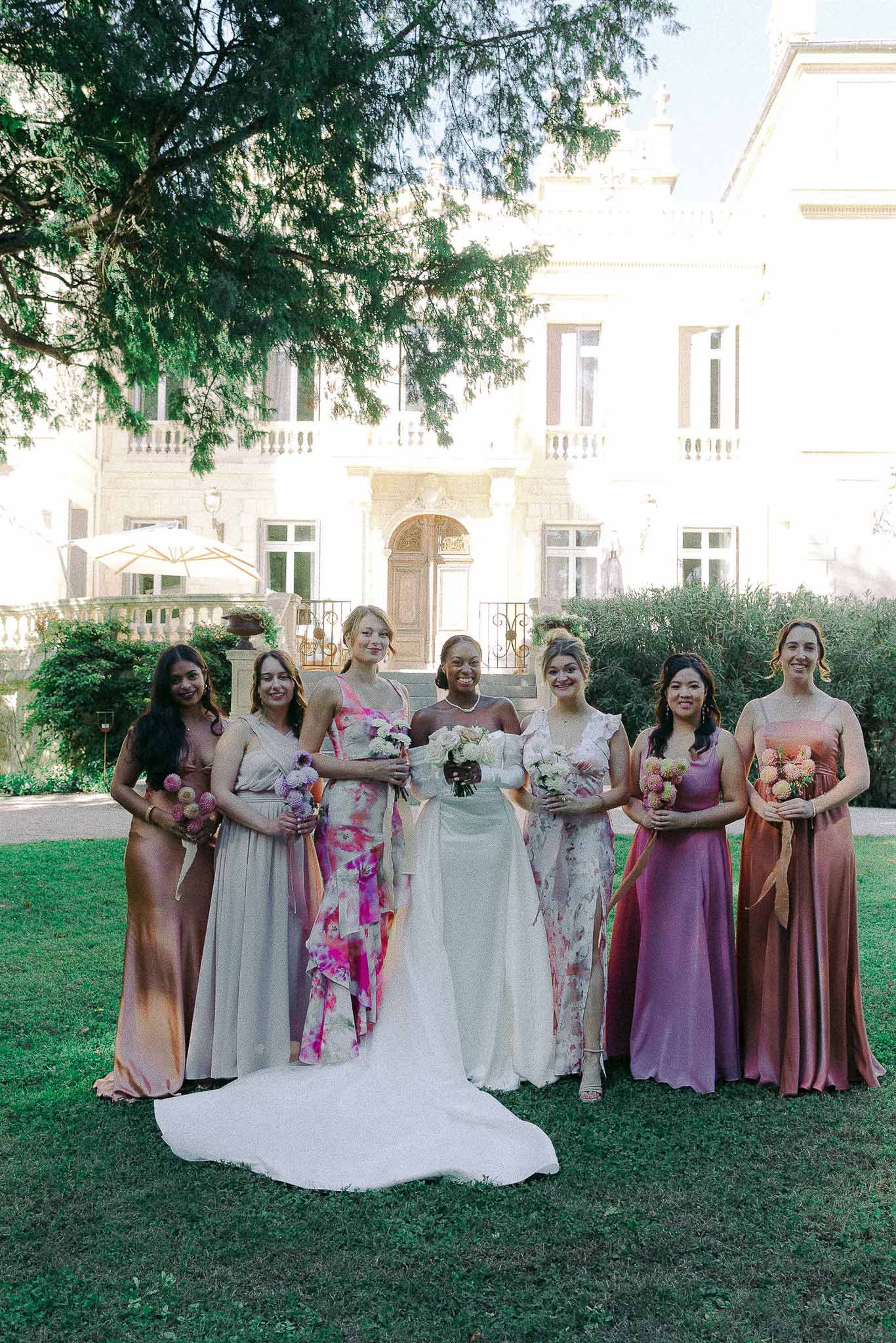 Bride with seven bridesmaids in group portrait on lawn in front of classical stone mansion