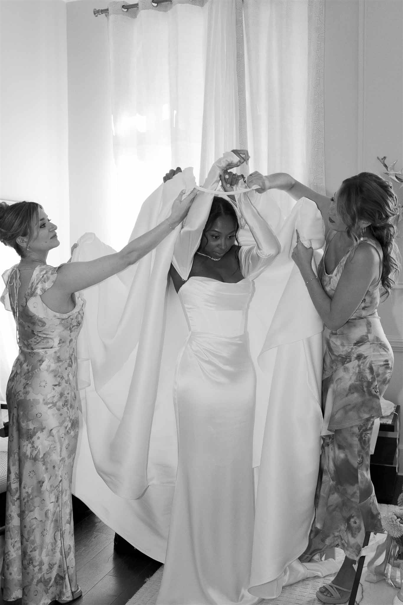 Bride having veil adjusted by attendants in bright bridal suite getting ready moment