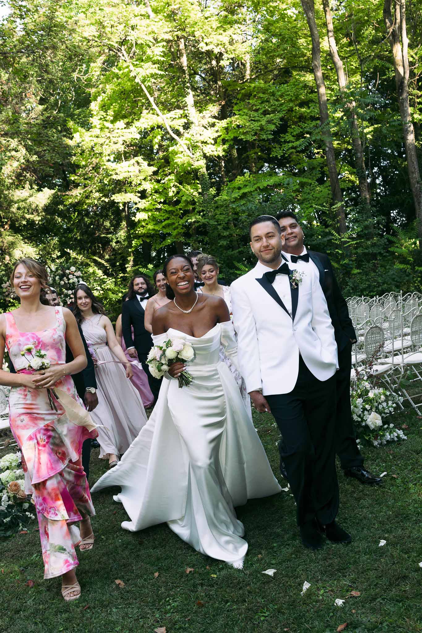 Bride and groom walking down garden aisle after ceremony with bridal party at outdoor wedding venue