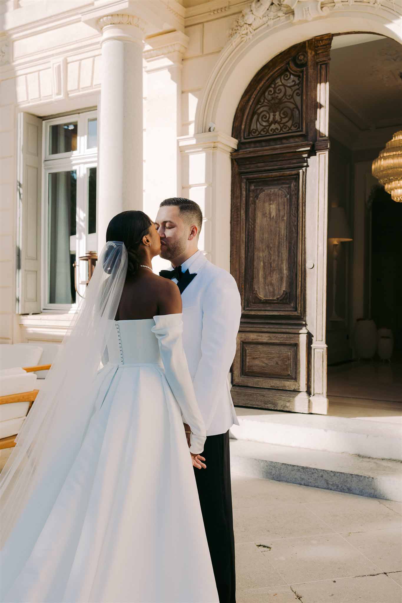 Bride and groom sharing first kiss in classical mansion hallway with neoclassical architecture