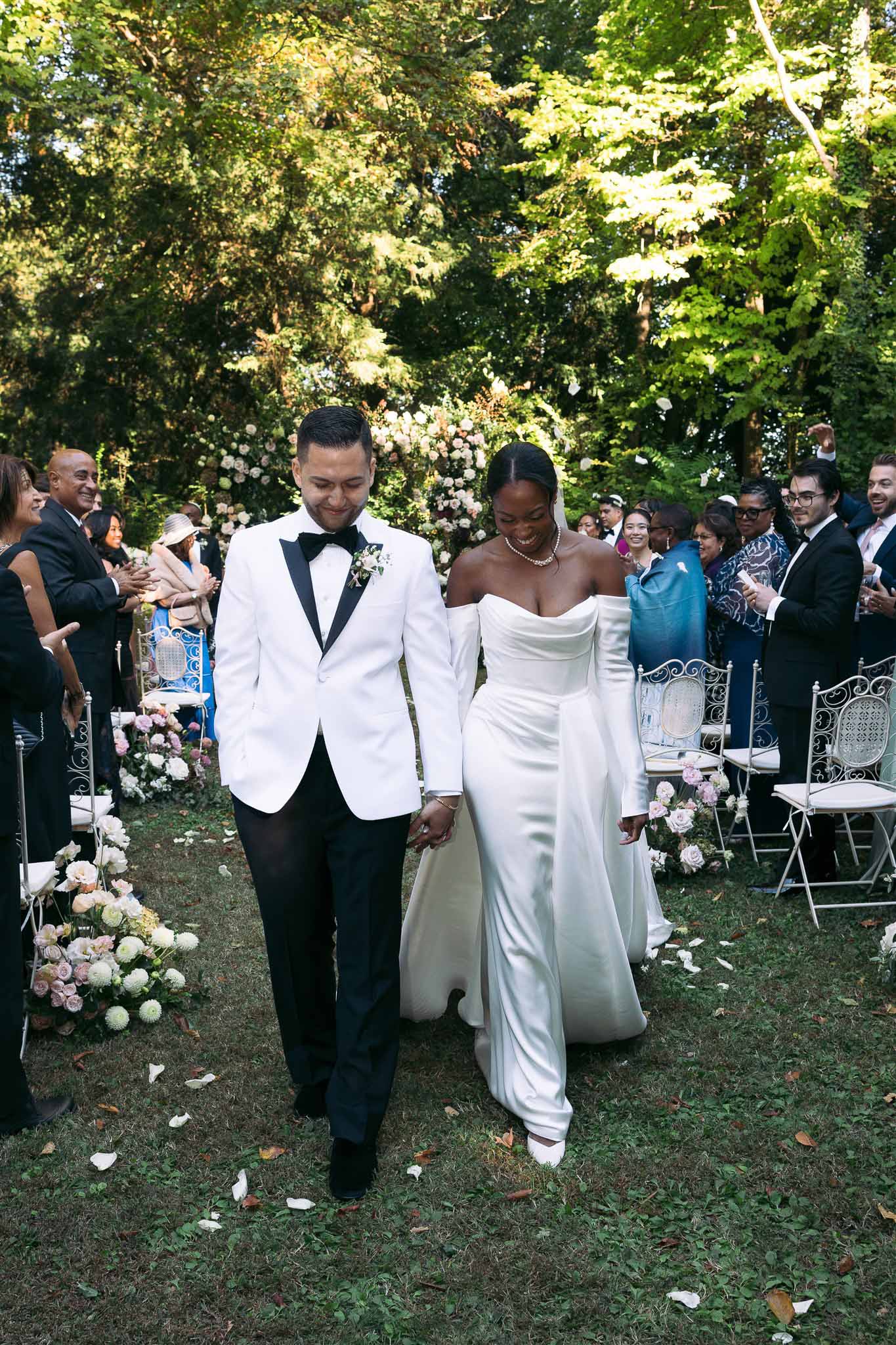 Bride and groom walking down aisle during outdoor garden ceremony with guests applauding