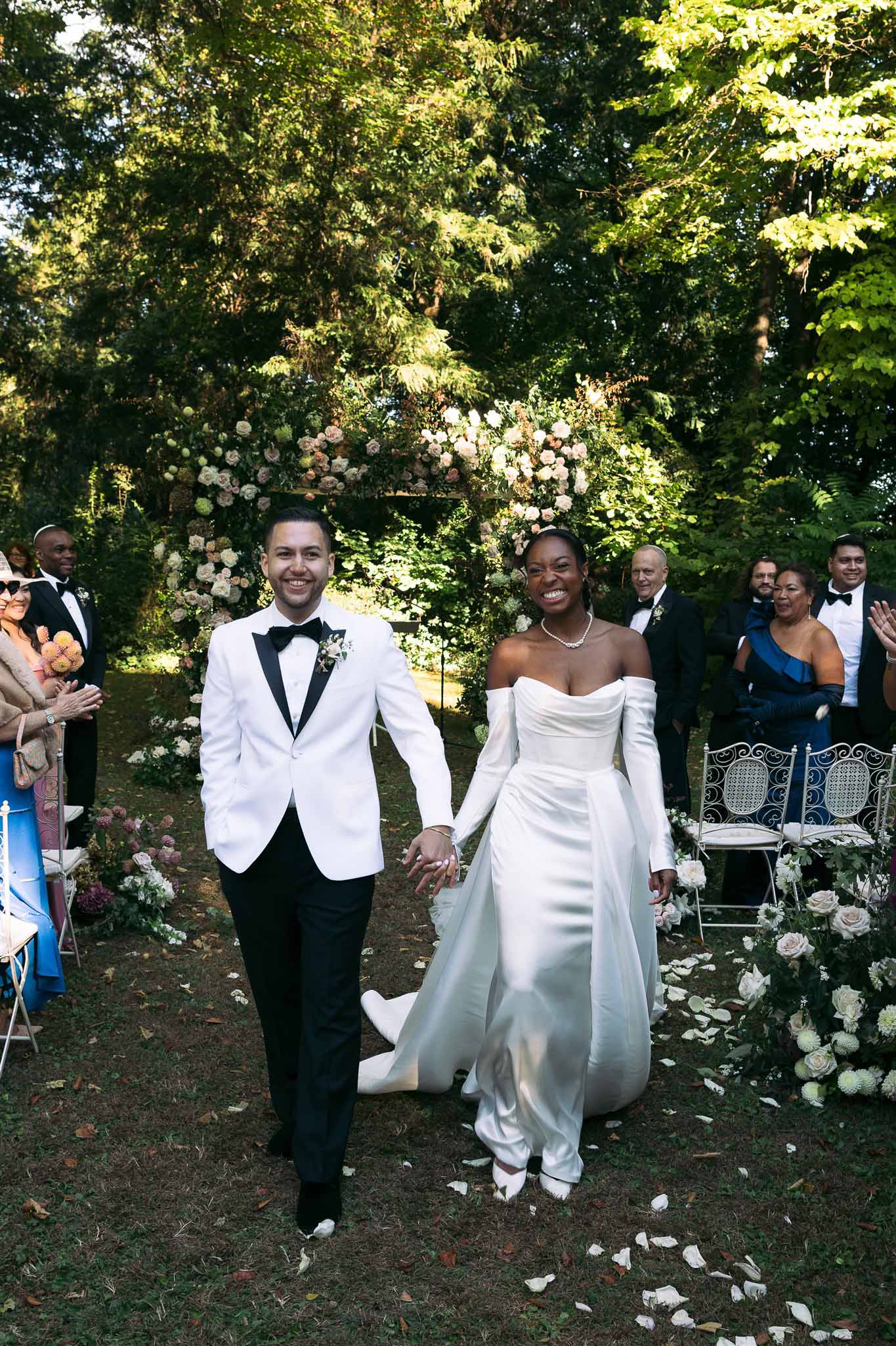 Bride and groom walking down aisle after ceremony in garden setting with floral arbor and seated guests