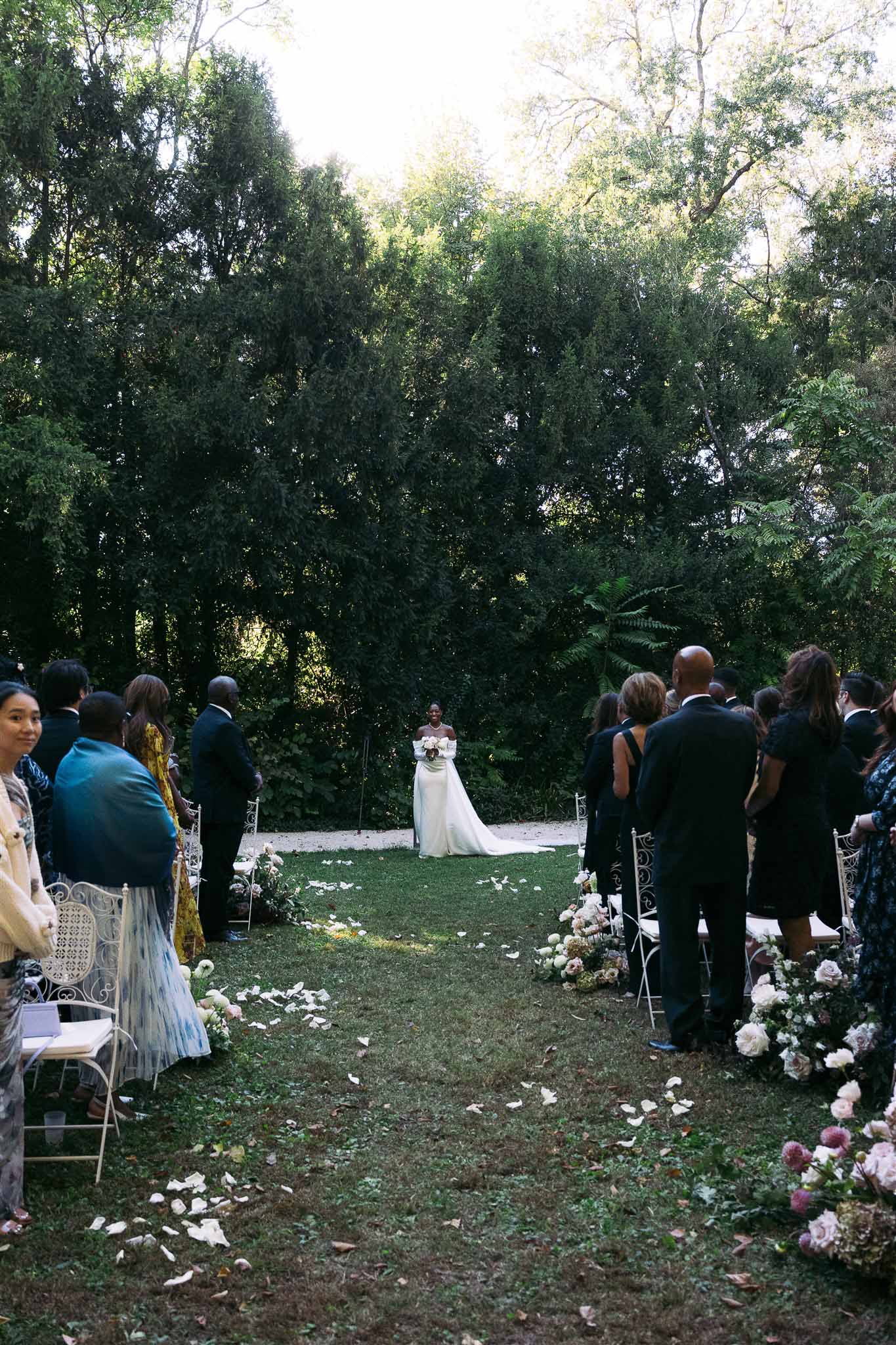 Outdoor wedding ceremony with bride at altar in garden setting with guests and floral arrangements