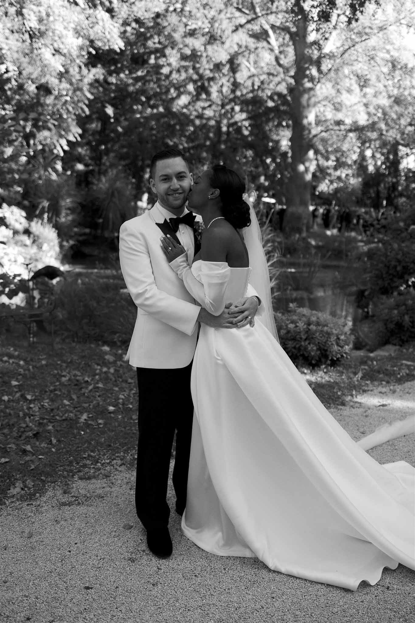 Bride and groom portrait in formal attire standing on garden path surrounded by trees