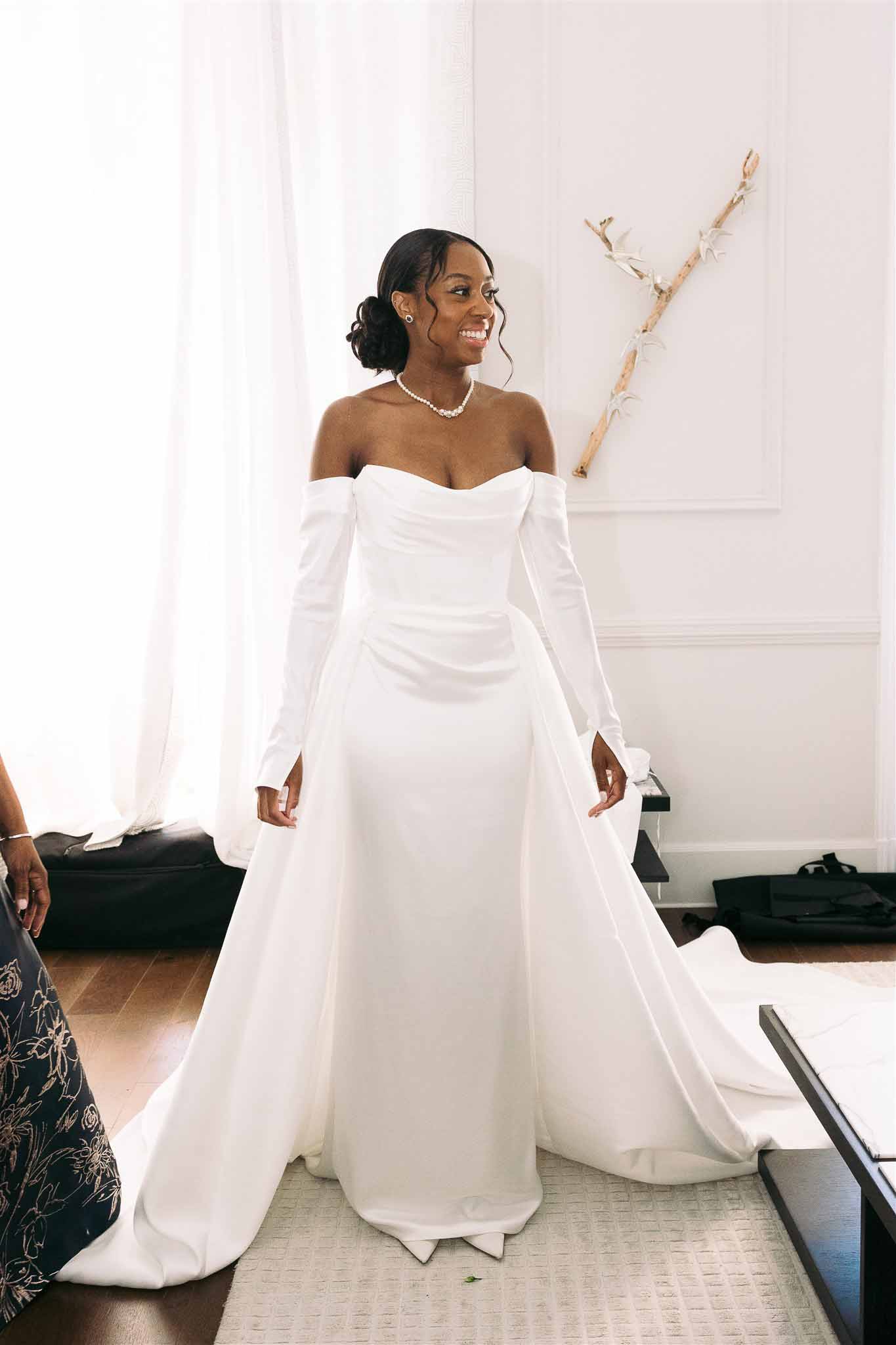 Bride in ivory off-shoulder gown with pearl accessories in bridal suite during portrait session