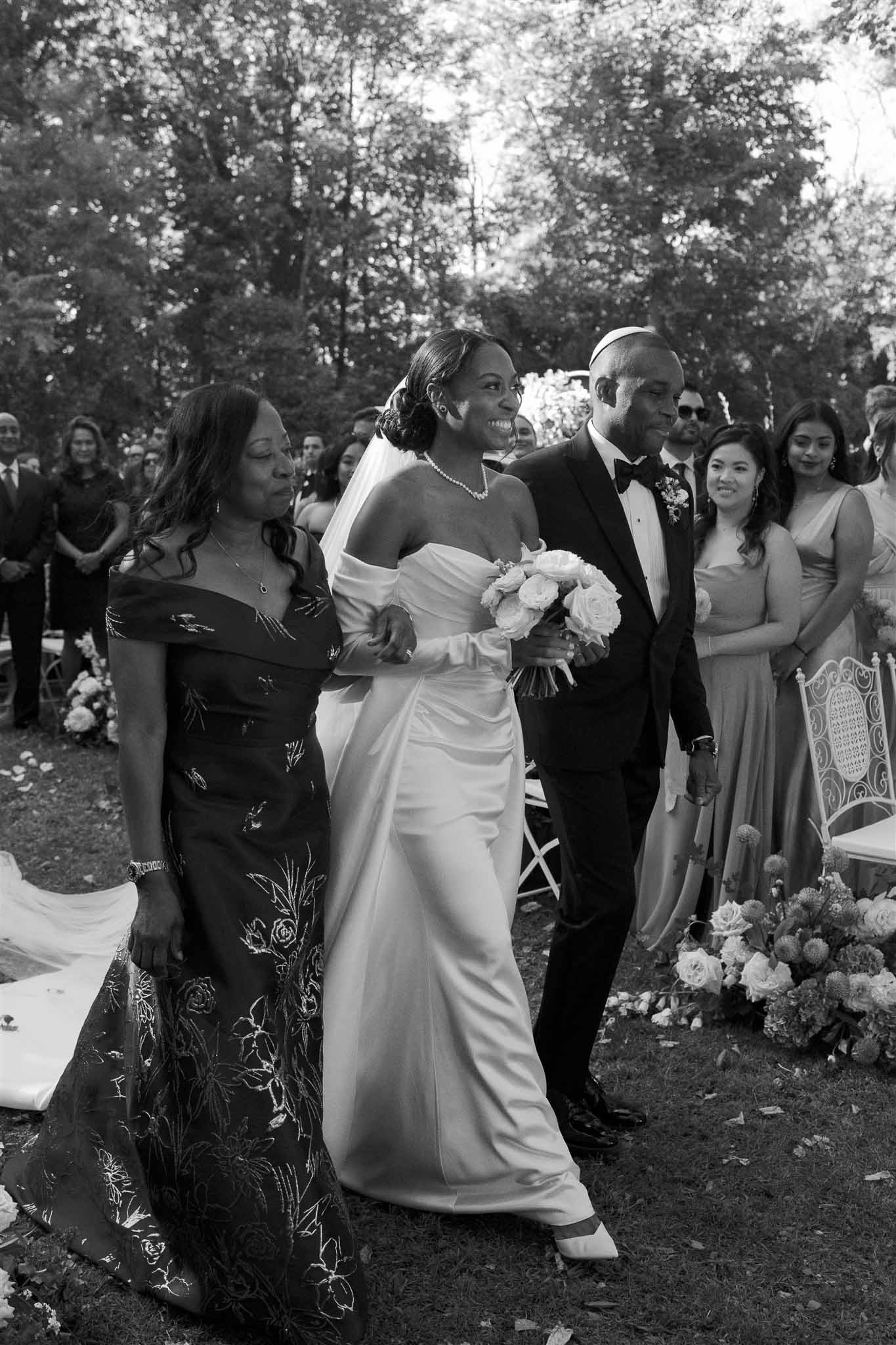 Bride and groom walking down aisle at outdoor woodland garden ceremony with guests flanking processional