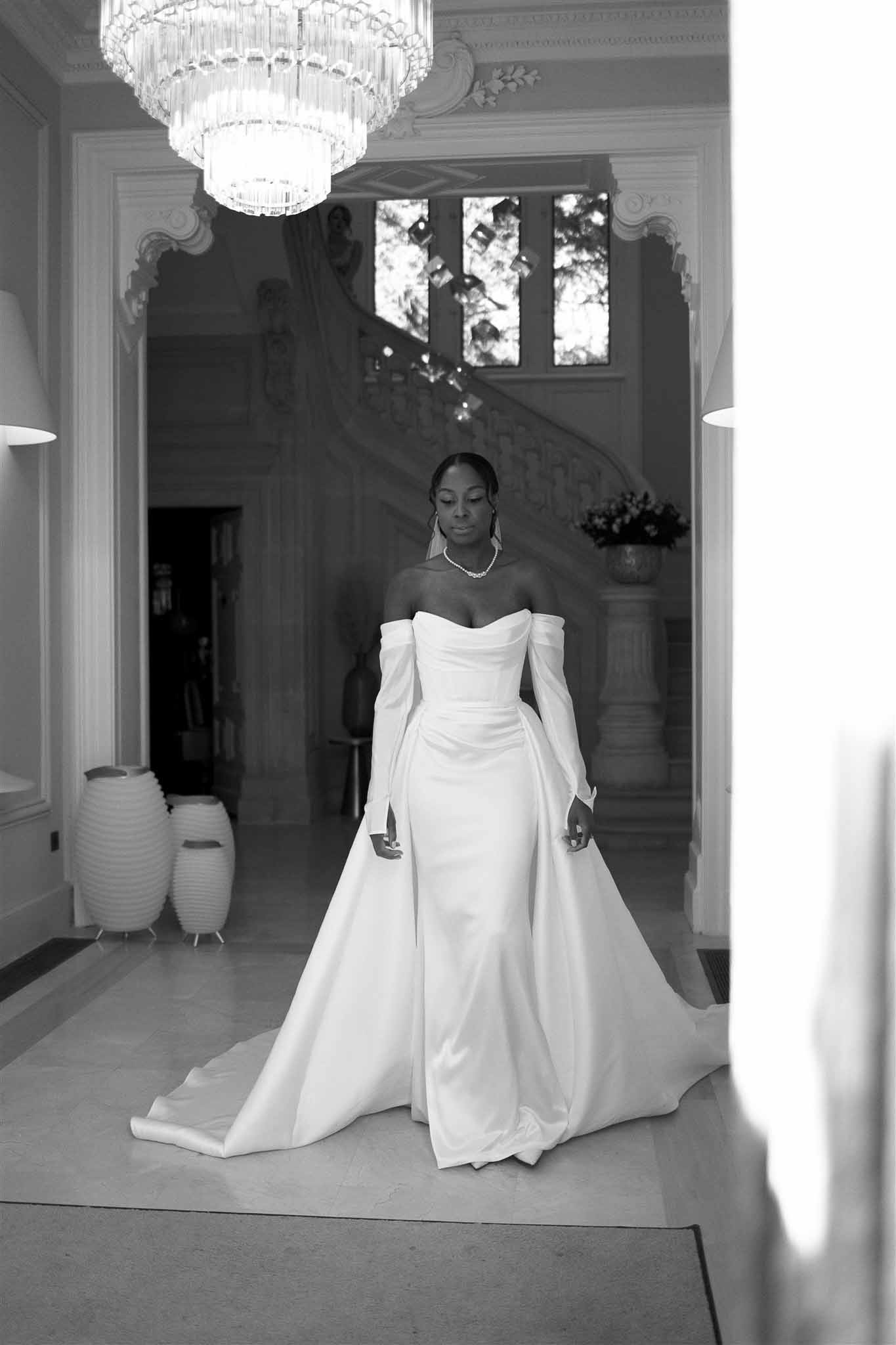 Bride in wedding gown standing in elegant neoclassical interior hallway with crystal chandelier