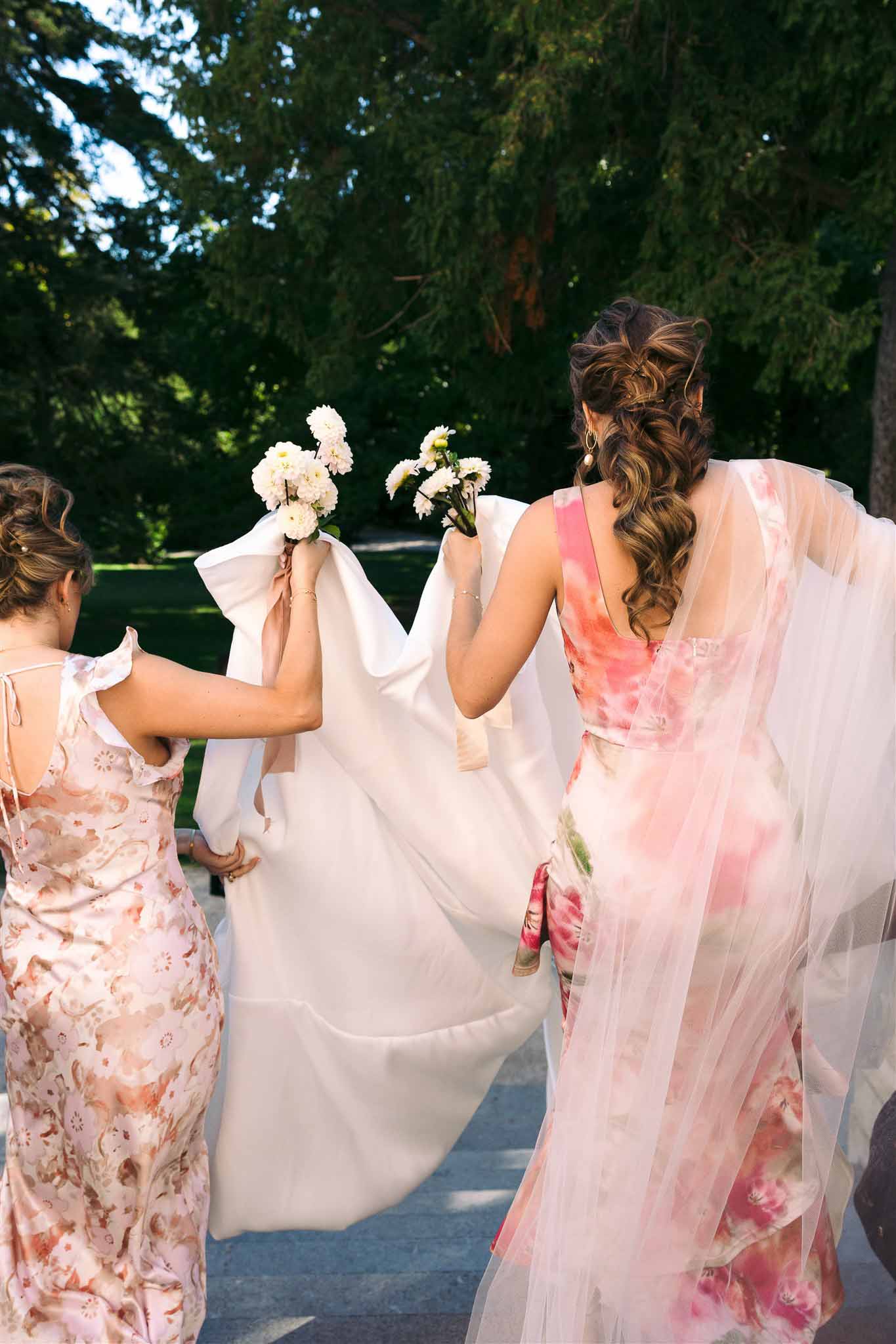 Bride and bridesmaids walking through garden pathway with bouquets and flowing veil
