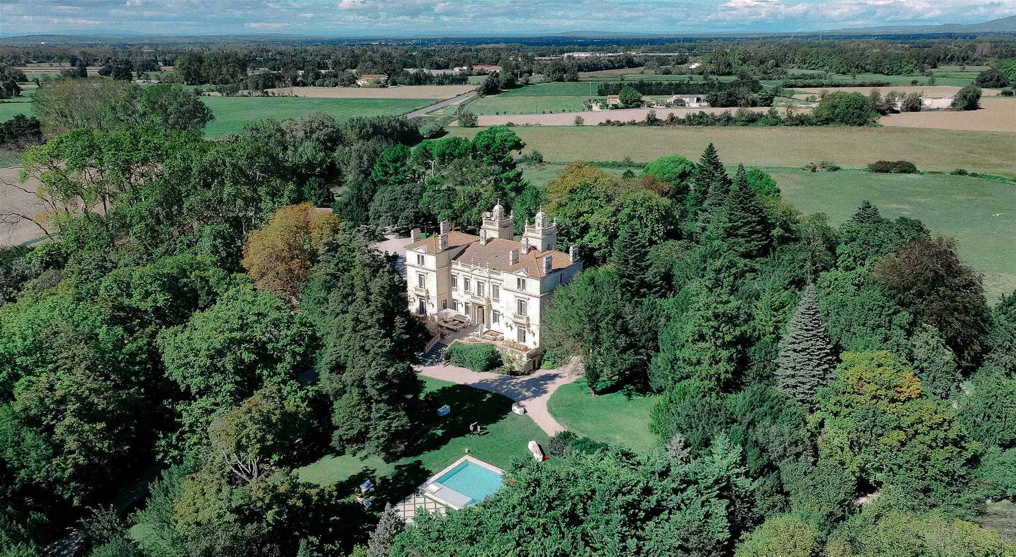 Aerial view of neoclassical château wedding venue with pool and manicured grounds surrounded by woodland